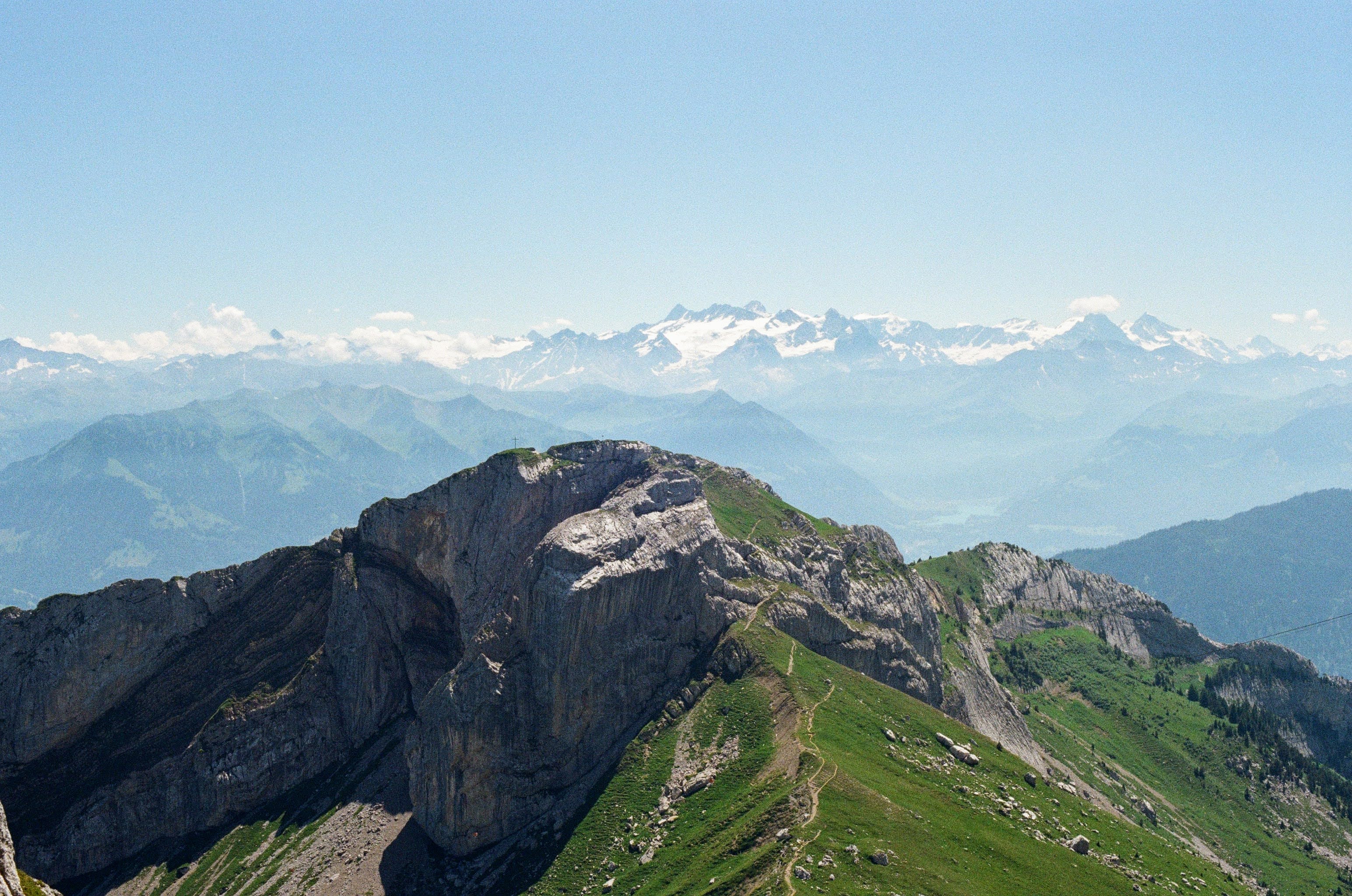 Snow capped mountains line the background of the shot, under a blue sky. In the foreground, a lower rocky peak is present.