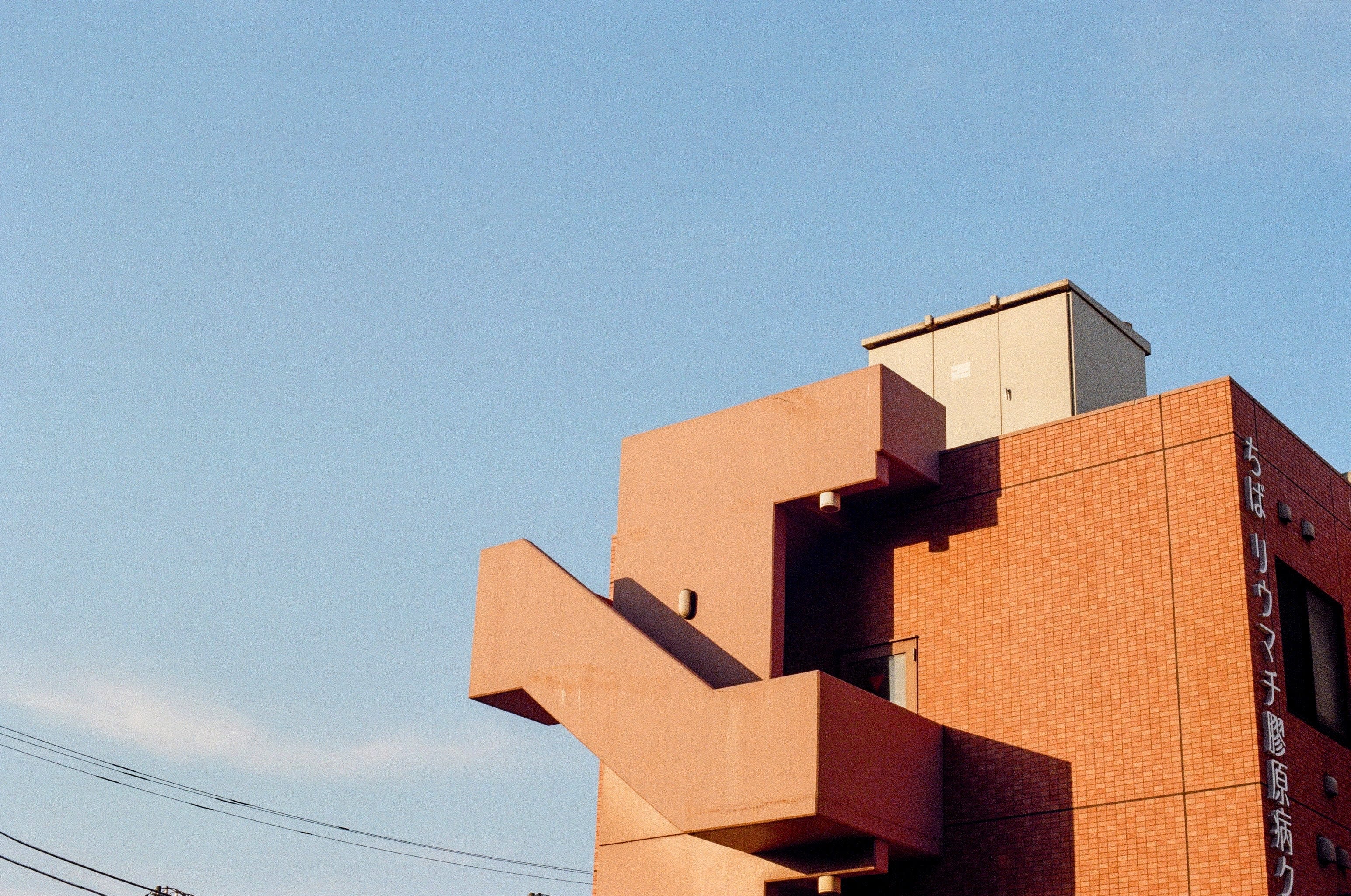Clear blue skies in the background, with an orange brick building in the lower left corner of the frame. The stairs case of the building wraps around the exterior, illuminated by the sunset's glow.