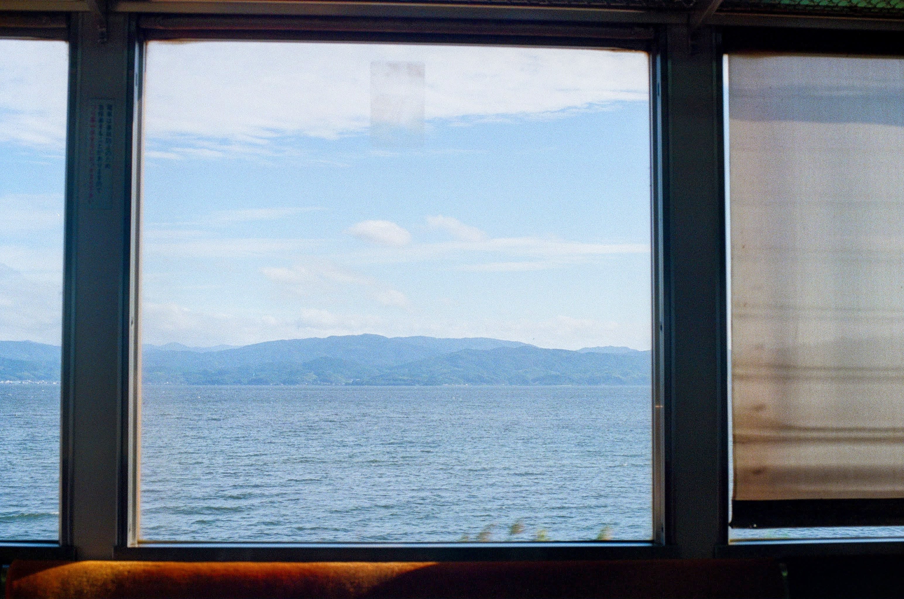 The view out a train window, looking over a lake at faint, distant mountains. Parts of the window frame are lit orange.