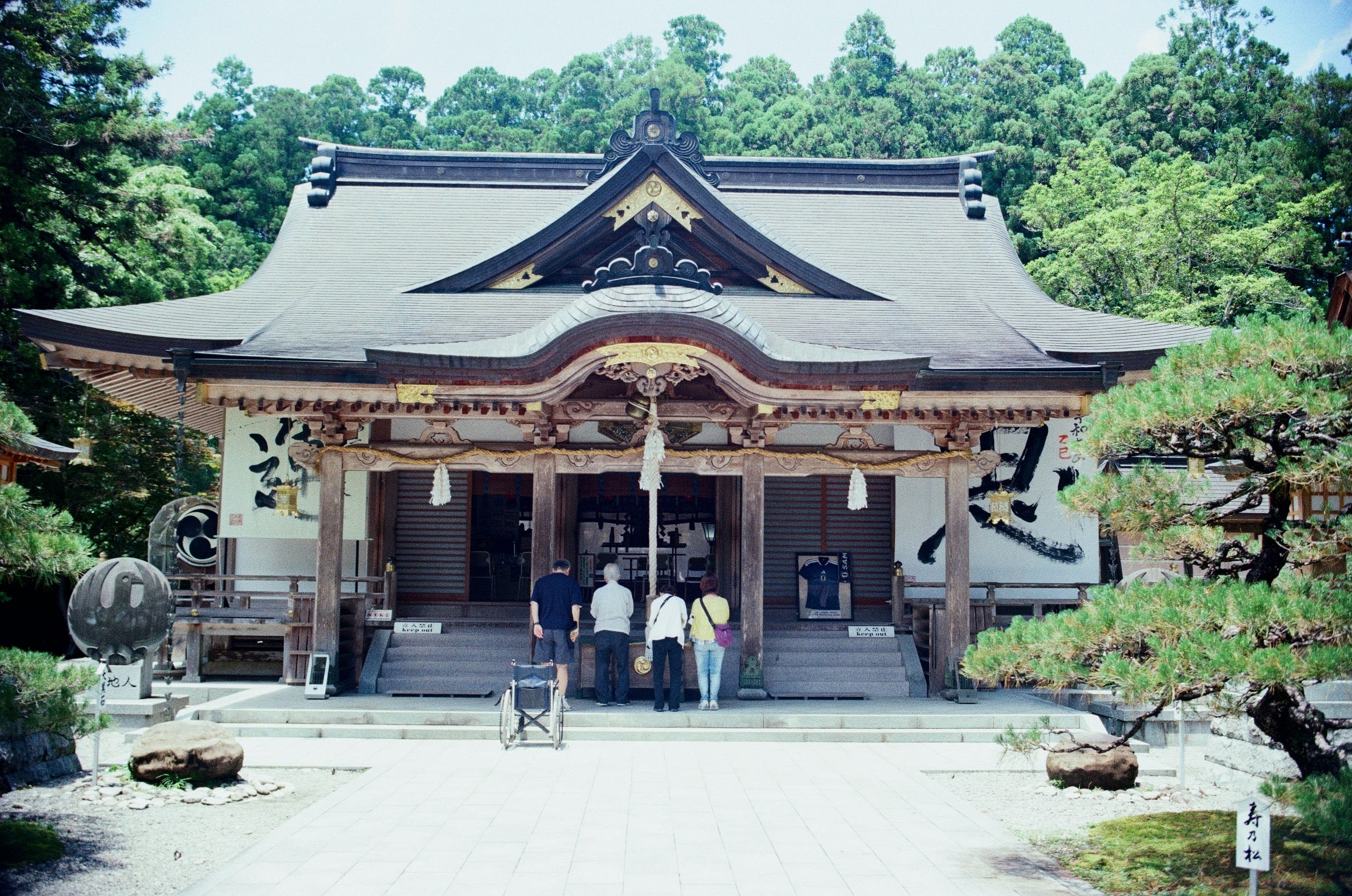 A group of four people pay respects at an old wooden Japanese temple.