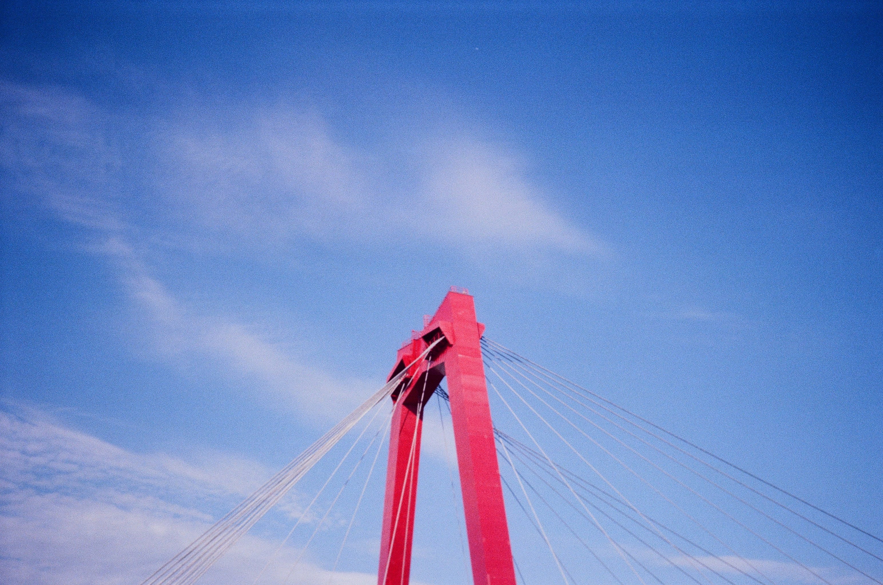 The red mast of a suspension bridge pokes up from the bottom of the frame into the blue sky.