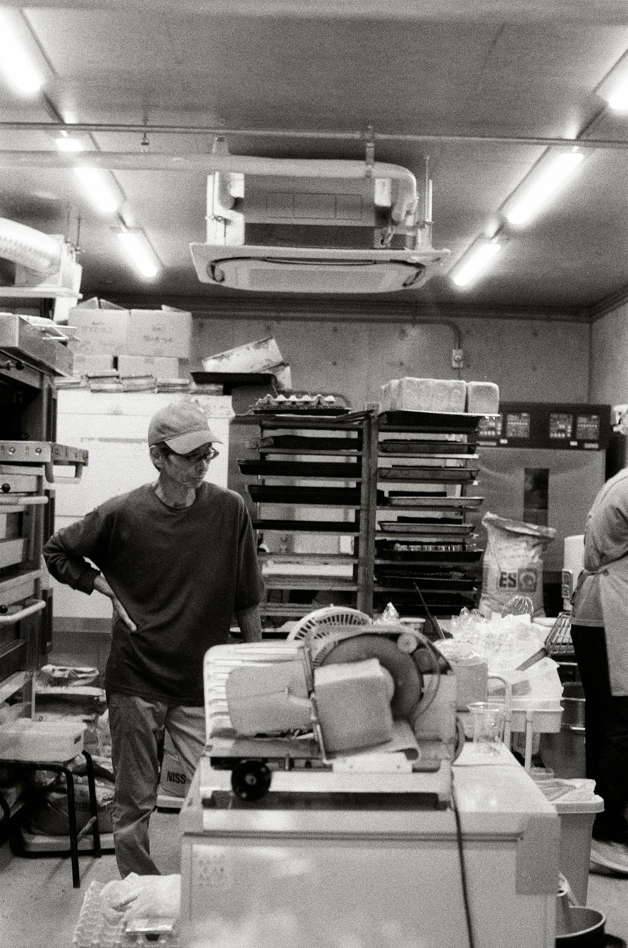 A man stands with one hand on his hip, looking at a messy bakery scene.