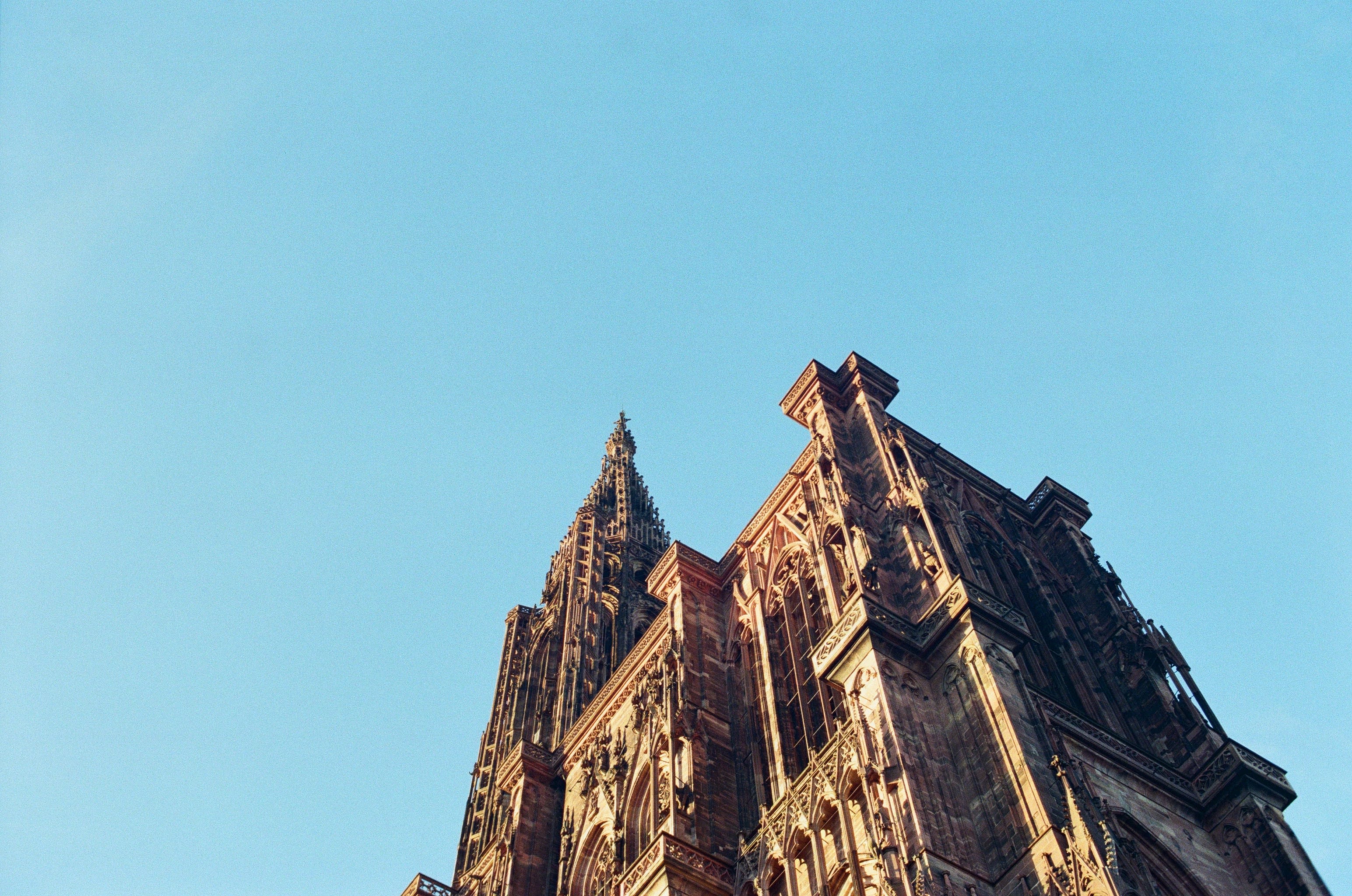 Looking up at a very decorated cathedral facade, the spire rises in the background with a flatter section of the roof in the foreground.