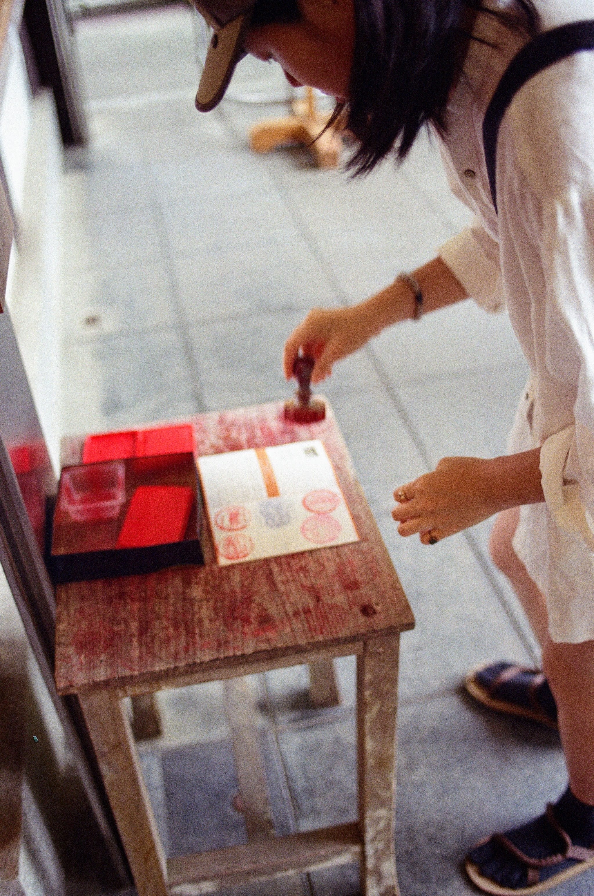 A lady crouches over a desk holding a red stamp. She is about to press it into a book that is opened on the desk before her.