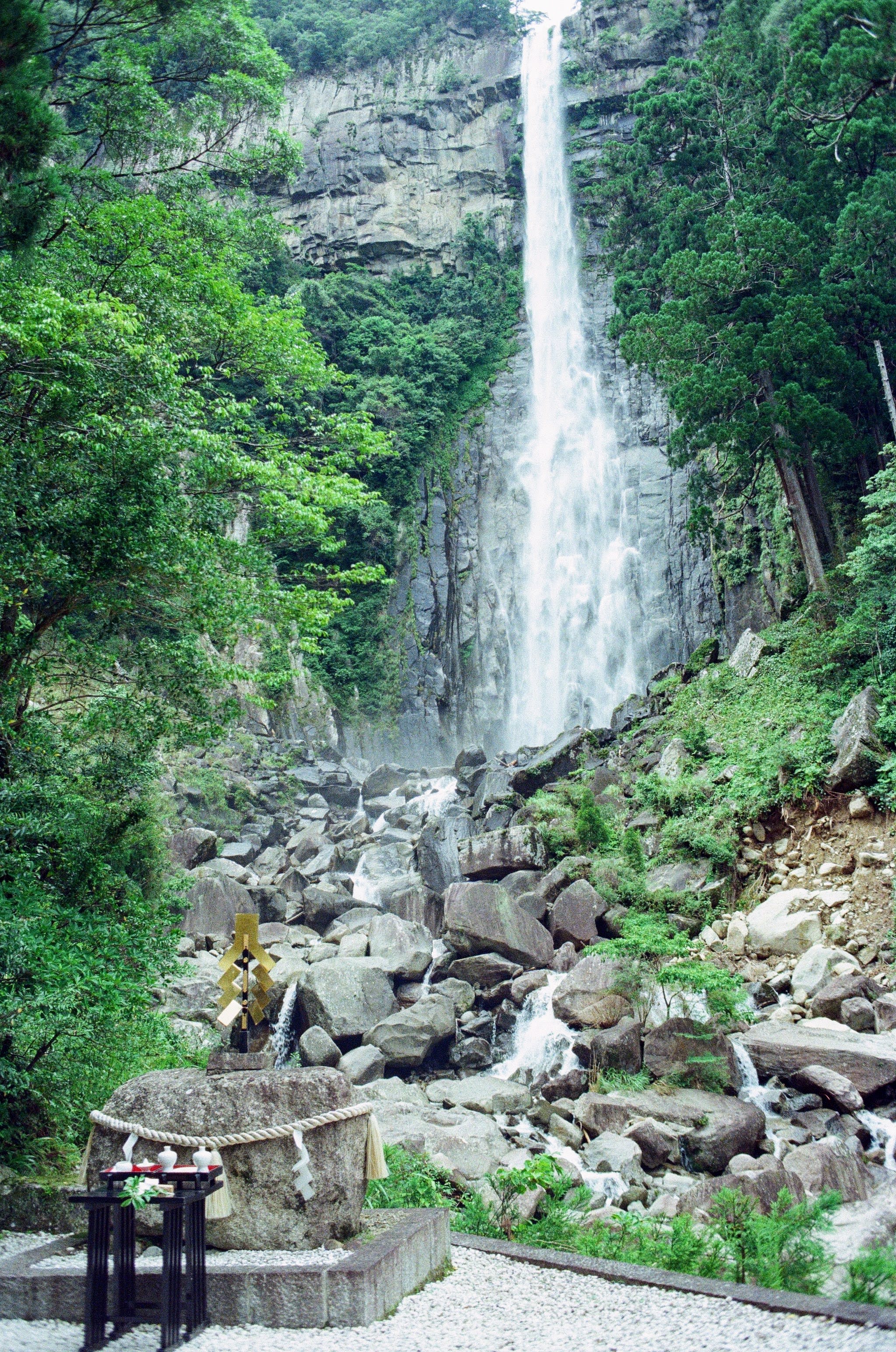 A waterfall comes down in the background with a stone shrine sitting on the land in the foreground.