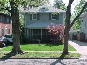 Front view of house with two trees, red flowering bush, bluish color siding and front porch