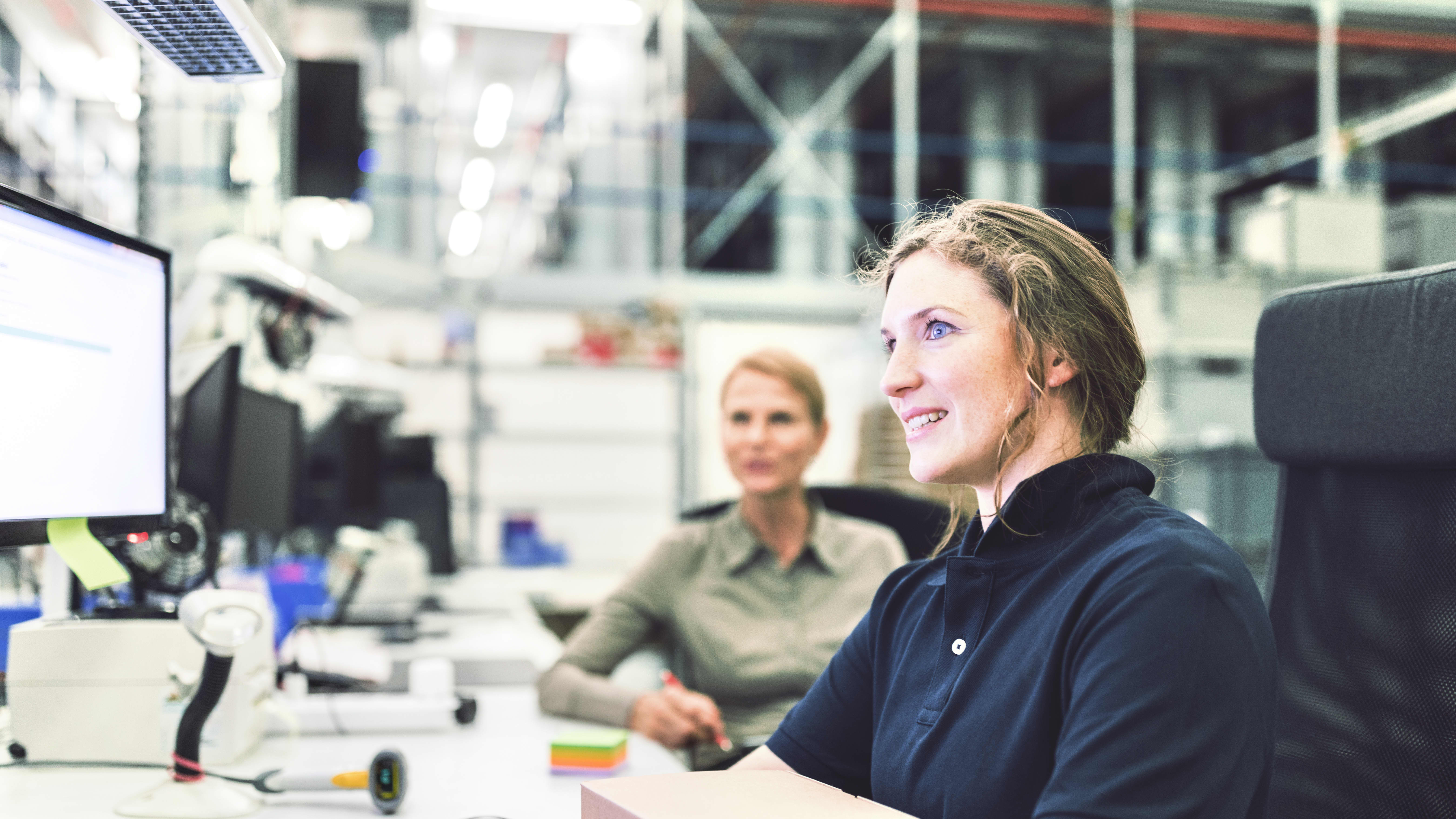 Karrieremöglichkeit “Supply Chain Manager:in”: Supply Chain Managerin sitzt gemeinsam mit einer Kollegin vor ihrem PC in einem Lagerbüro