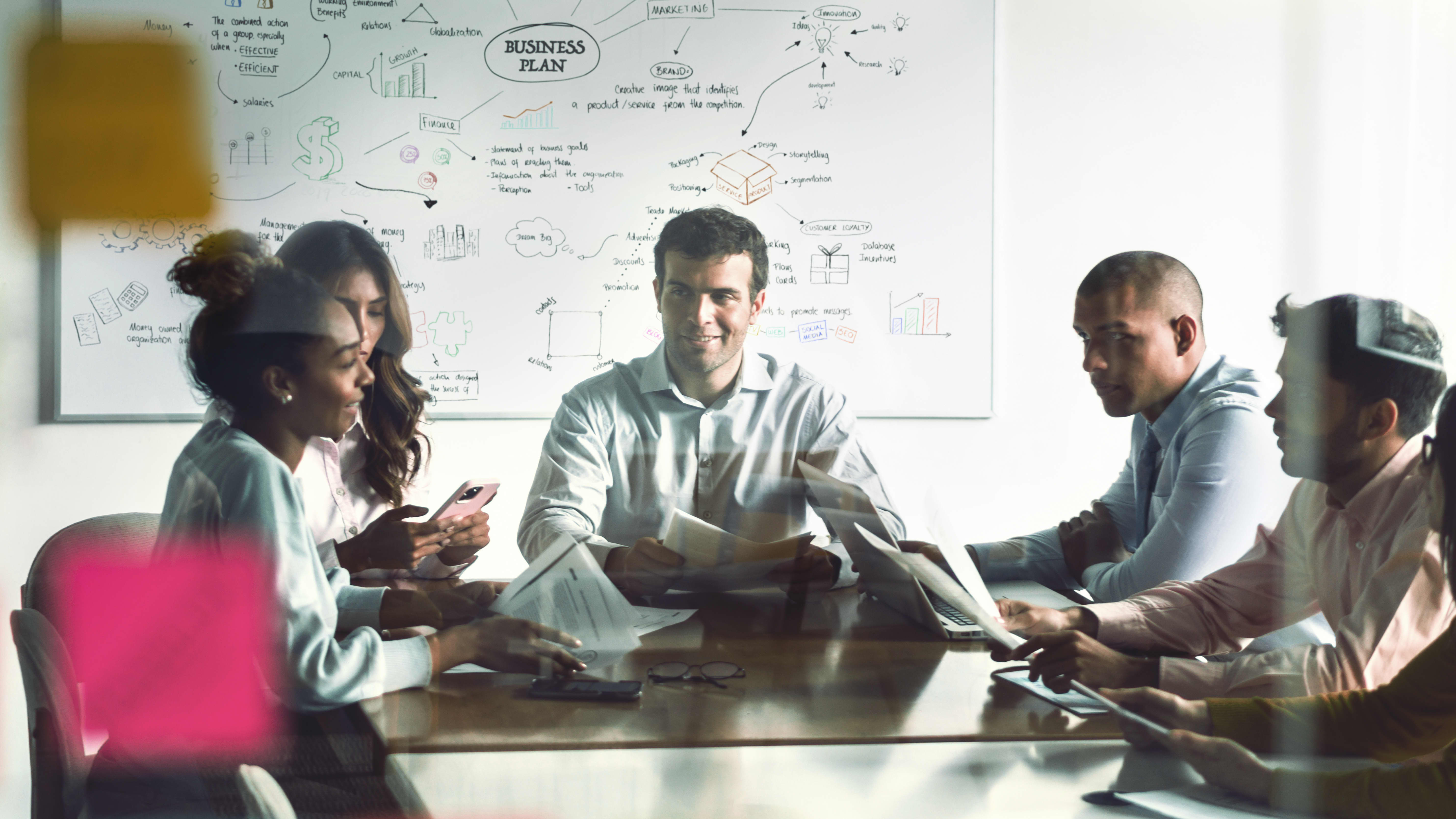 Karrieremöglichkeit “Costumer-Relationship-Manager:in”: Ein Team aus Costumer-Relationship-Manager:innen sitzt zusammen an einem Tisch und diskutiert über einen Business-Plan