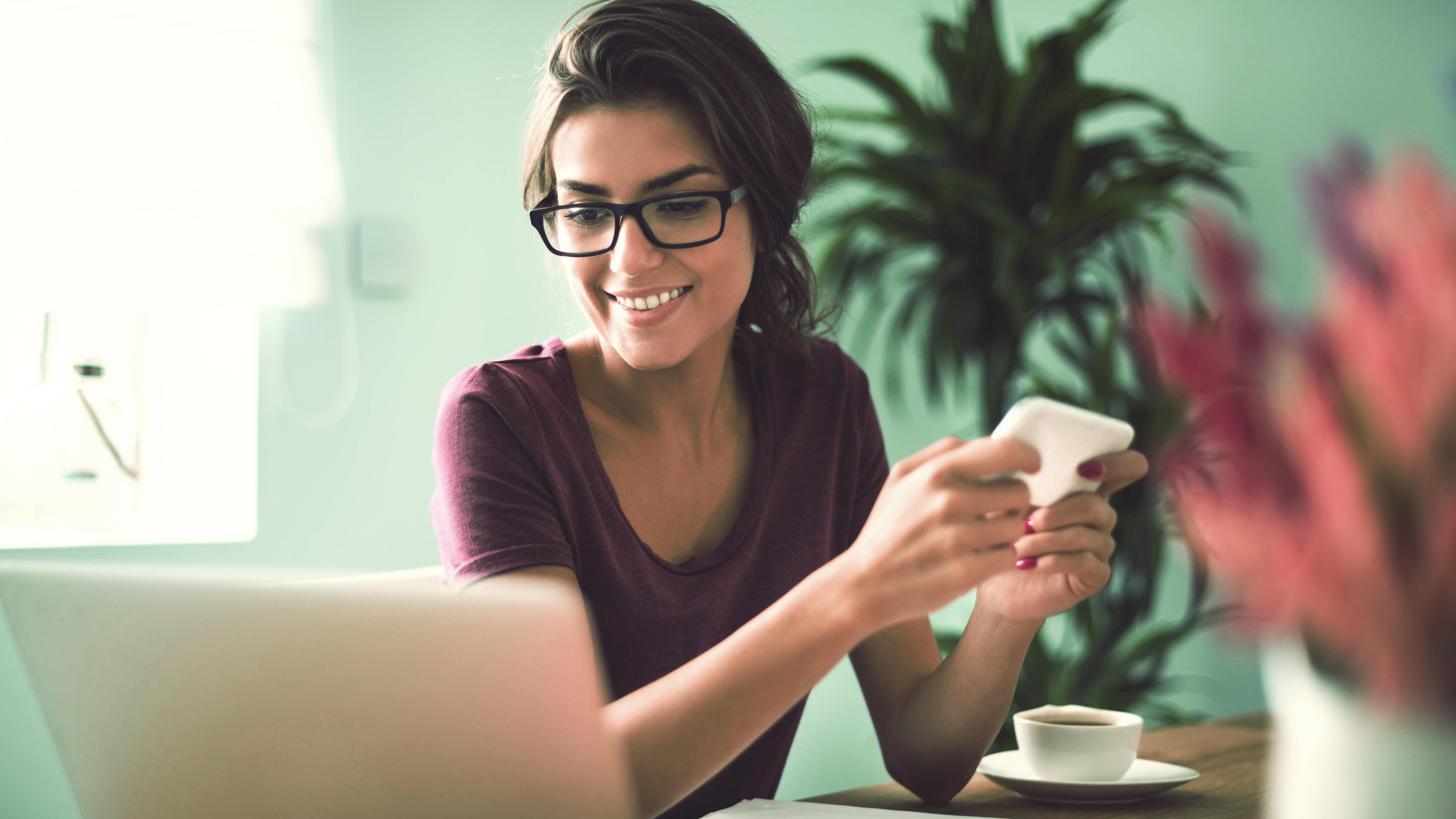Frau mit Smartphone vor Laptop