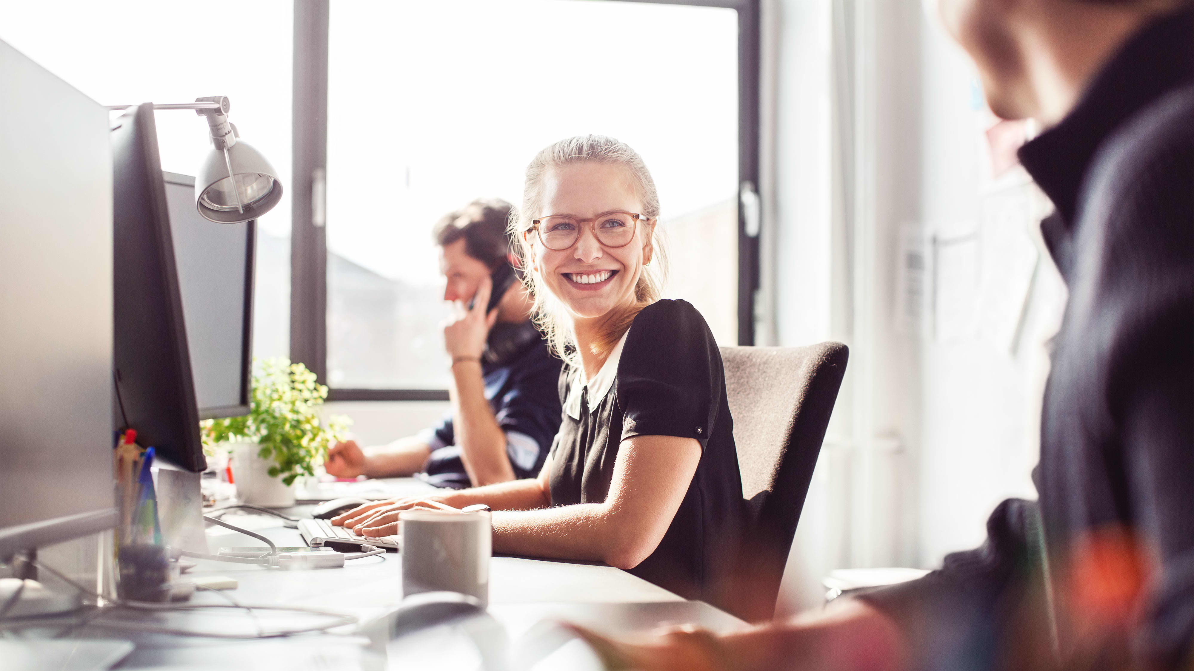 Karrieremöglichkeit “Projektleiter:in Digital”: Projektleiterin mit Brille sitzt mit Kolleg:innen im Büro