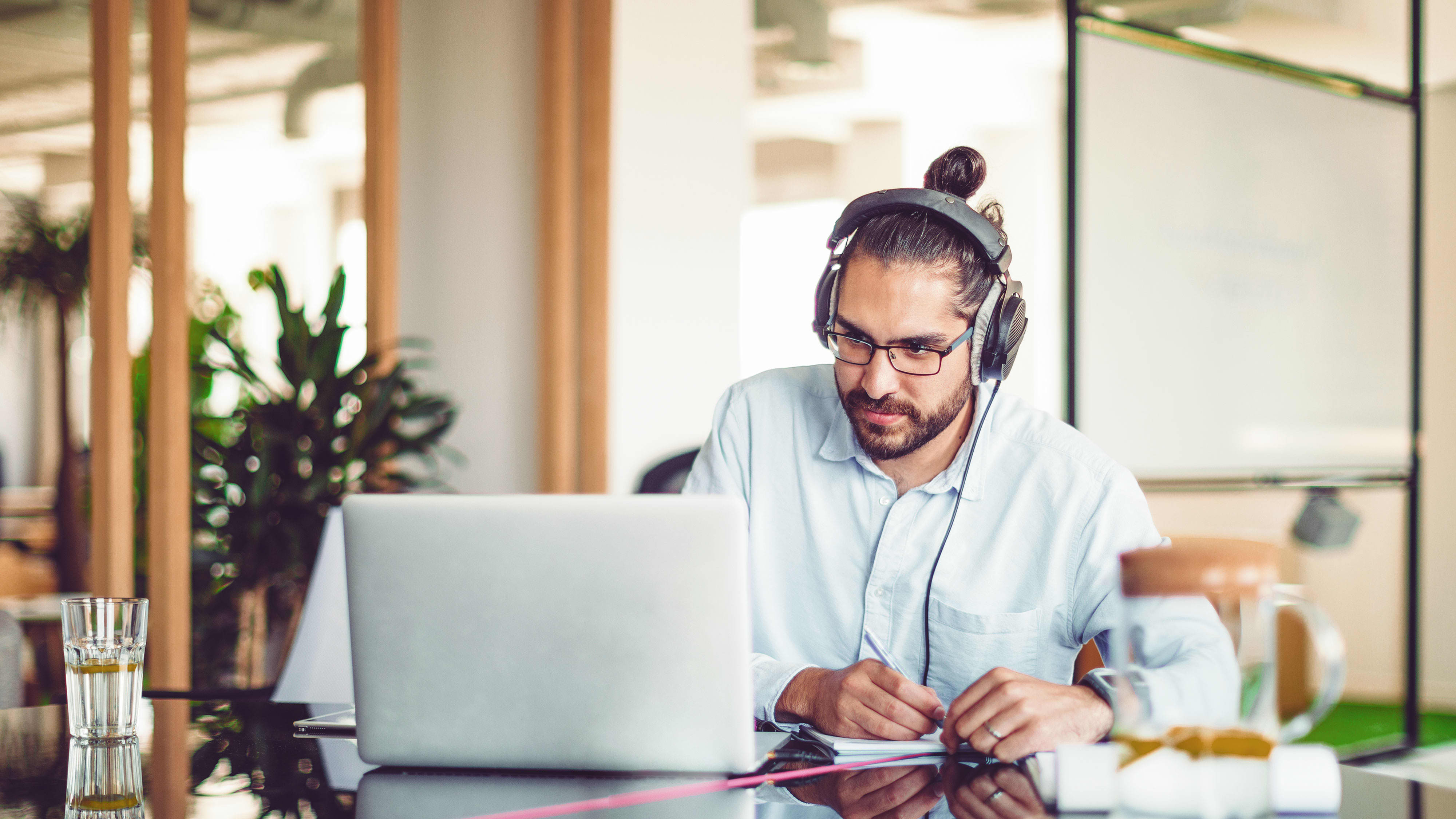 Karrieremöglichkeit “Content-Marketing-Manager:in”: Content-Manager mit Headset auf dem Kopf sitzt vor seinem PC und skizziert seine Ideen auf einem Zettel