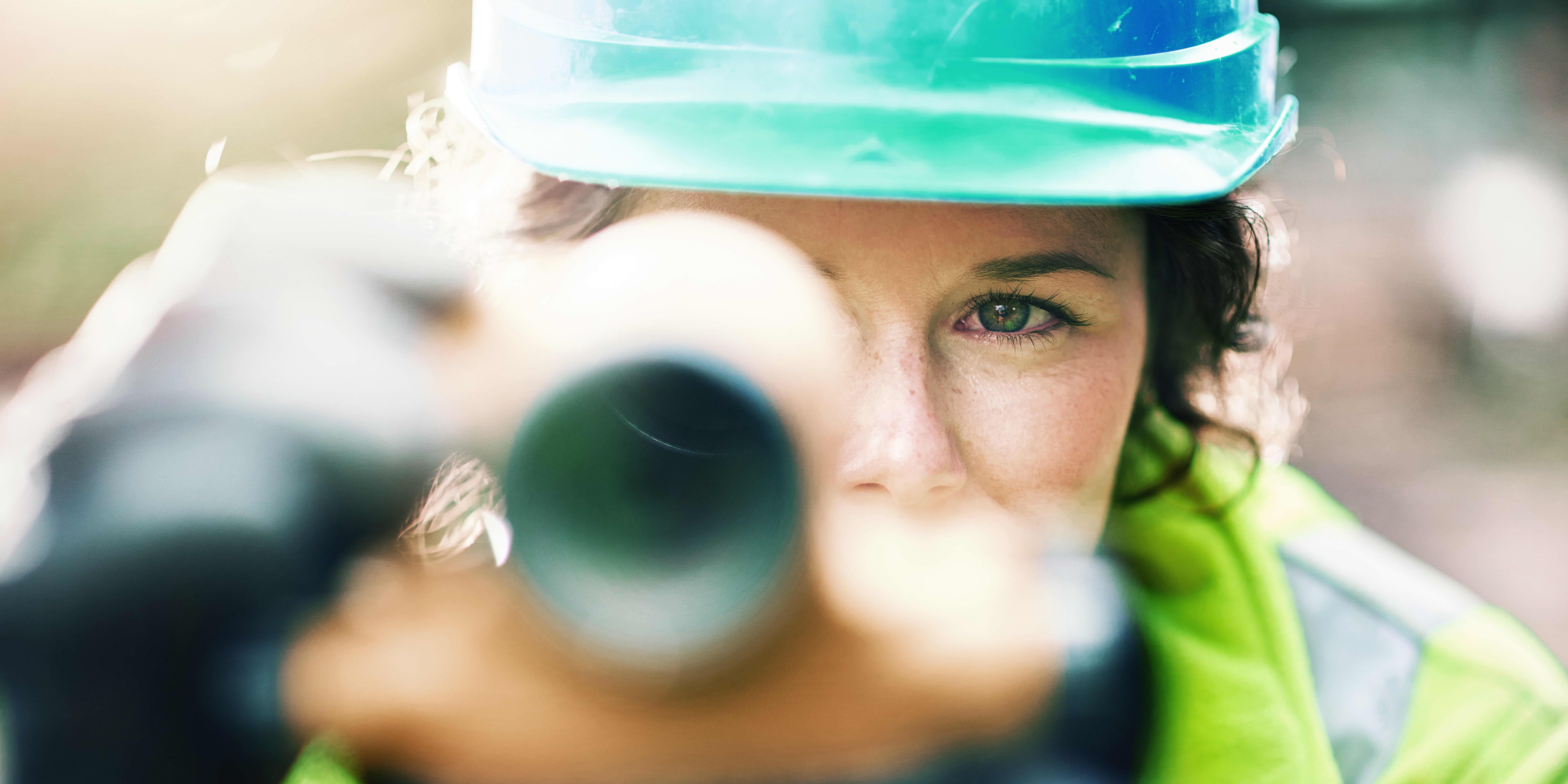 Karrieremöglichkeit “Bauingenieur:in”: Bauingenieurin auf einer Baustelle schaut durch ein Vermessungsgerät