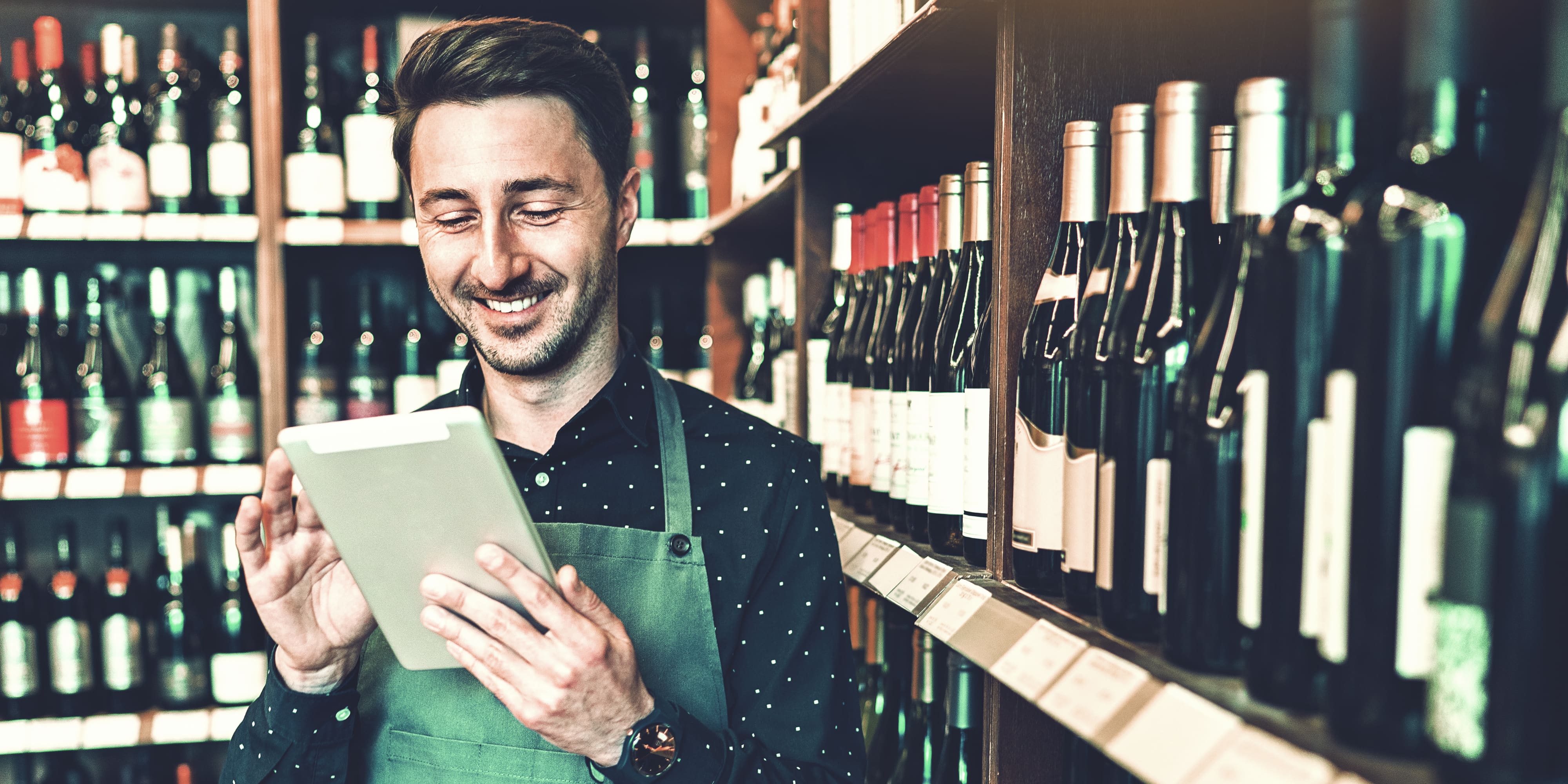 Mann mit Tablet vor dem Weinregal