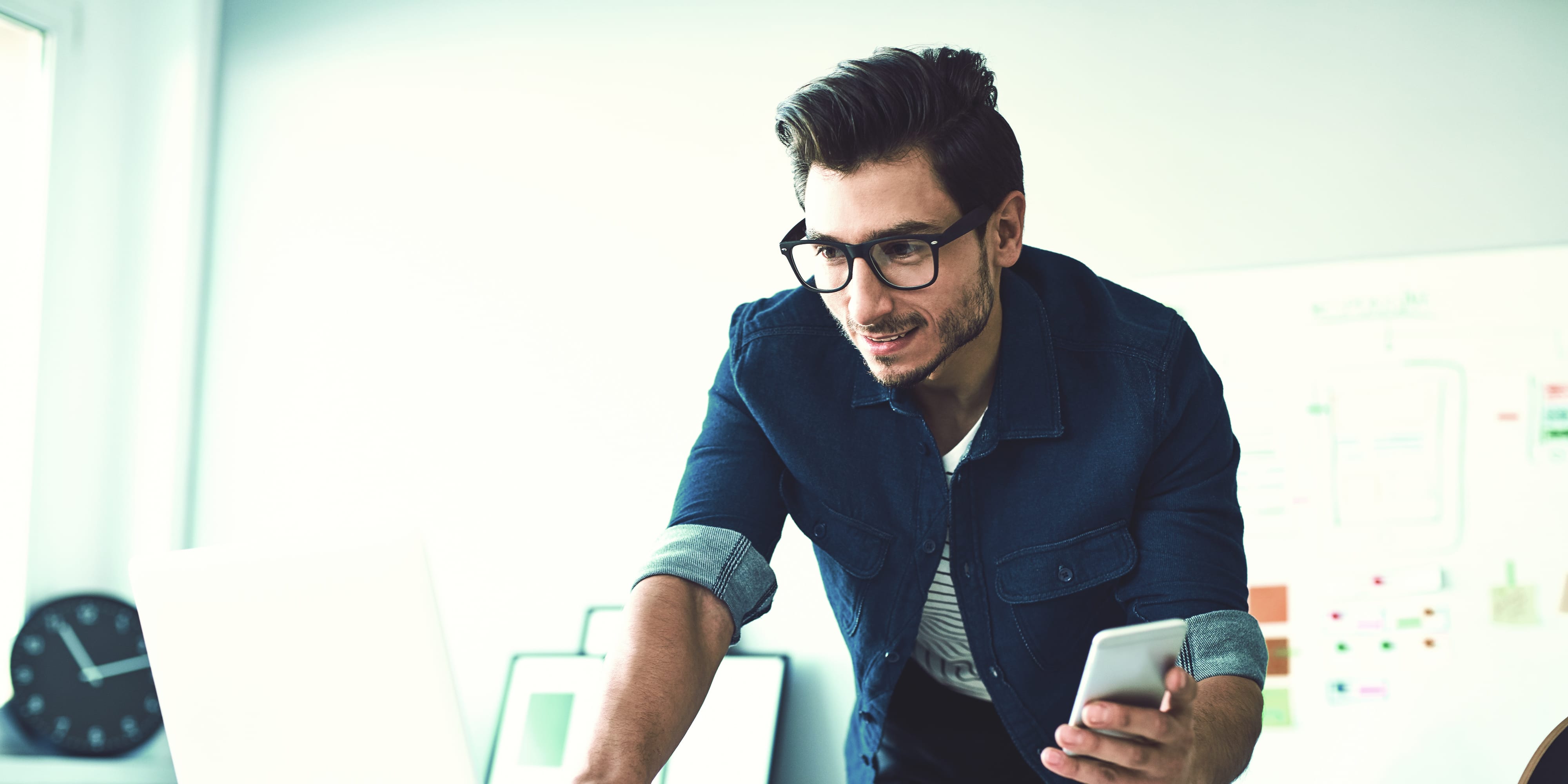 Mann mit Smartphone vor Laptop