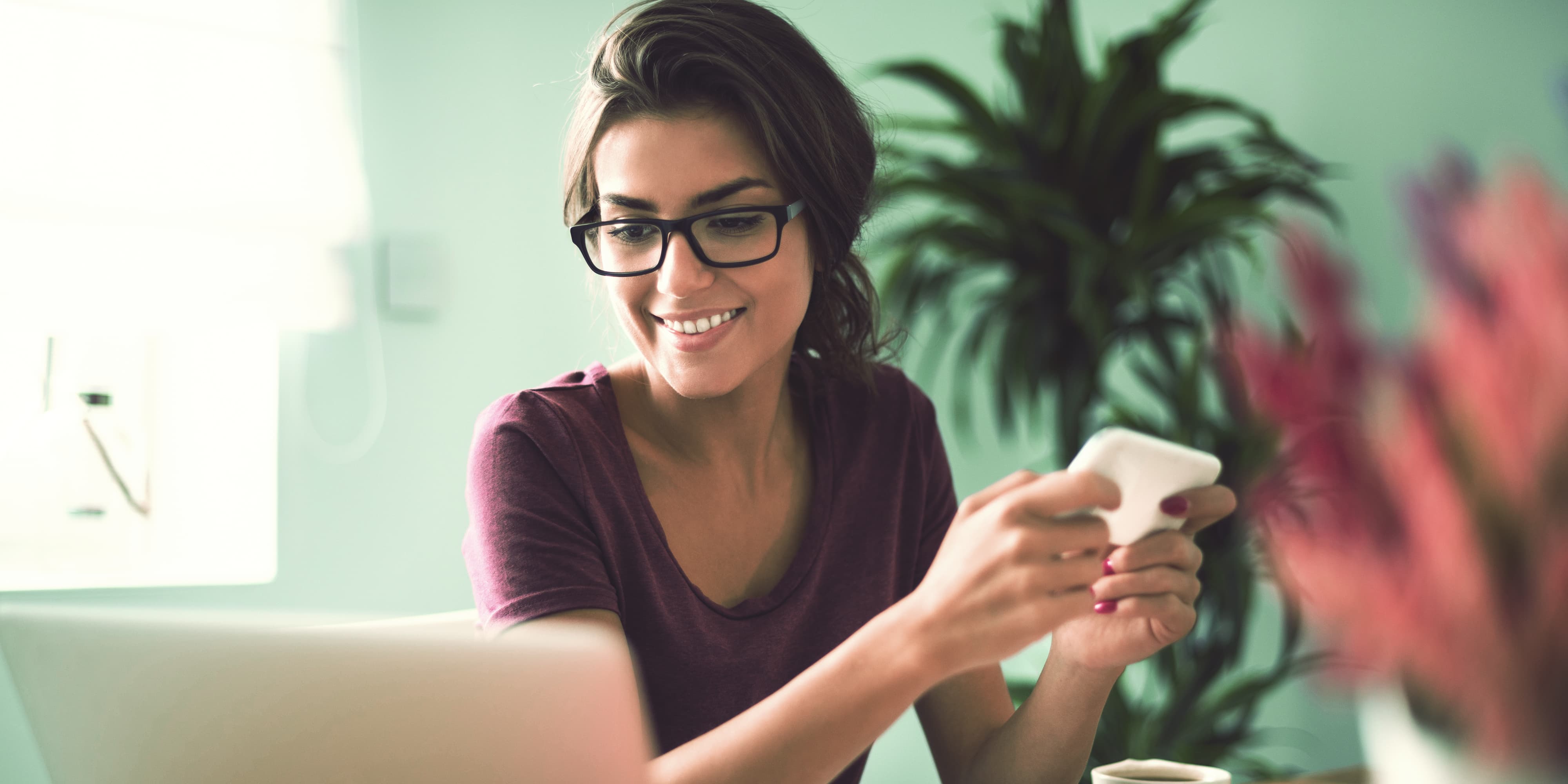 Frau mit Smartphone vor Laptop