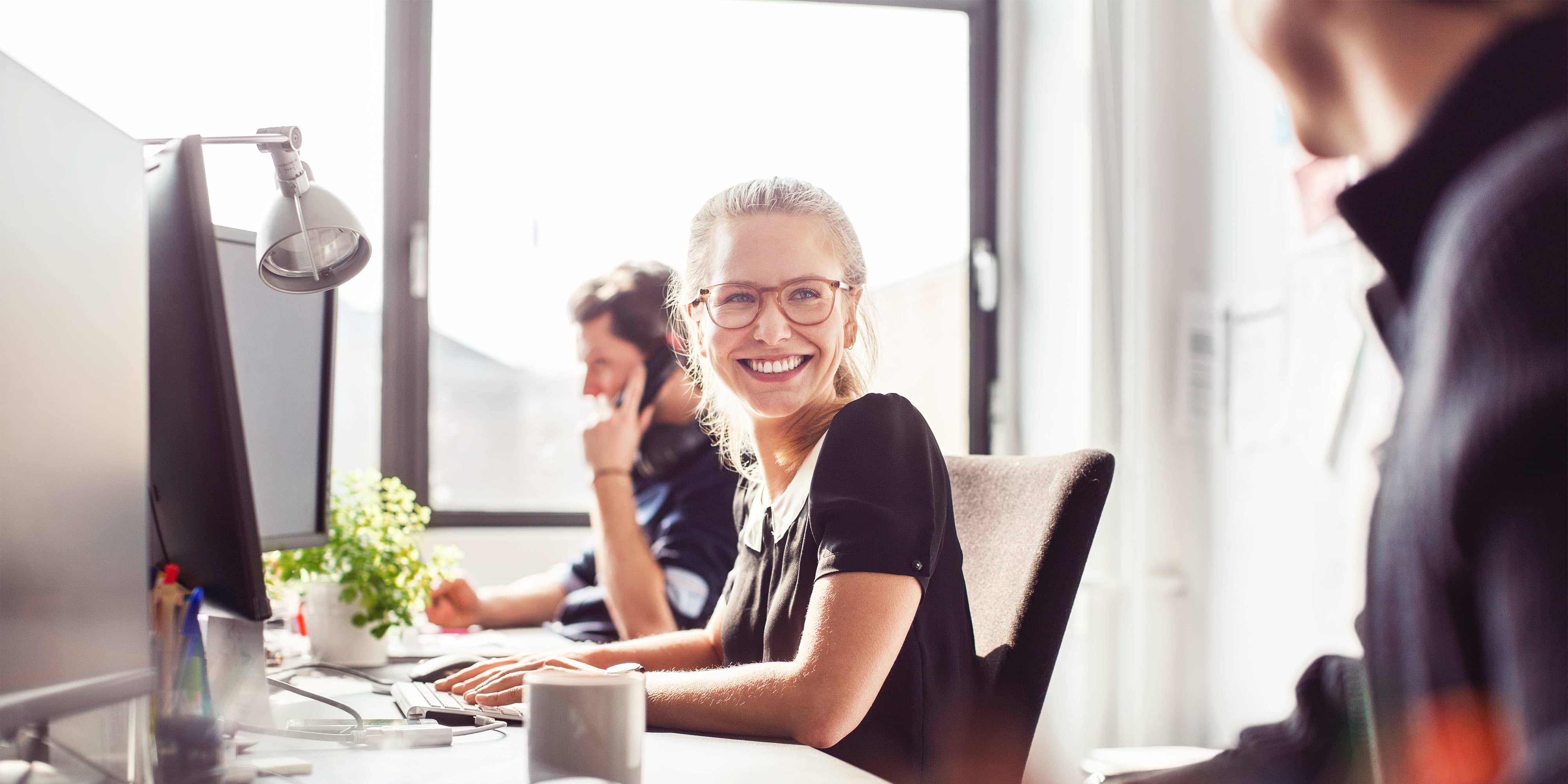 Karrieremöglichkeit “Projektleiter:in Digital”: Projektleiterin mit Brille sitzt mit Kolleg:innen im Büro