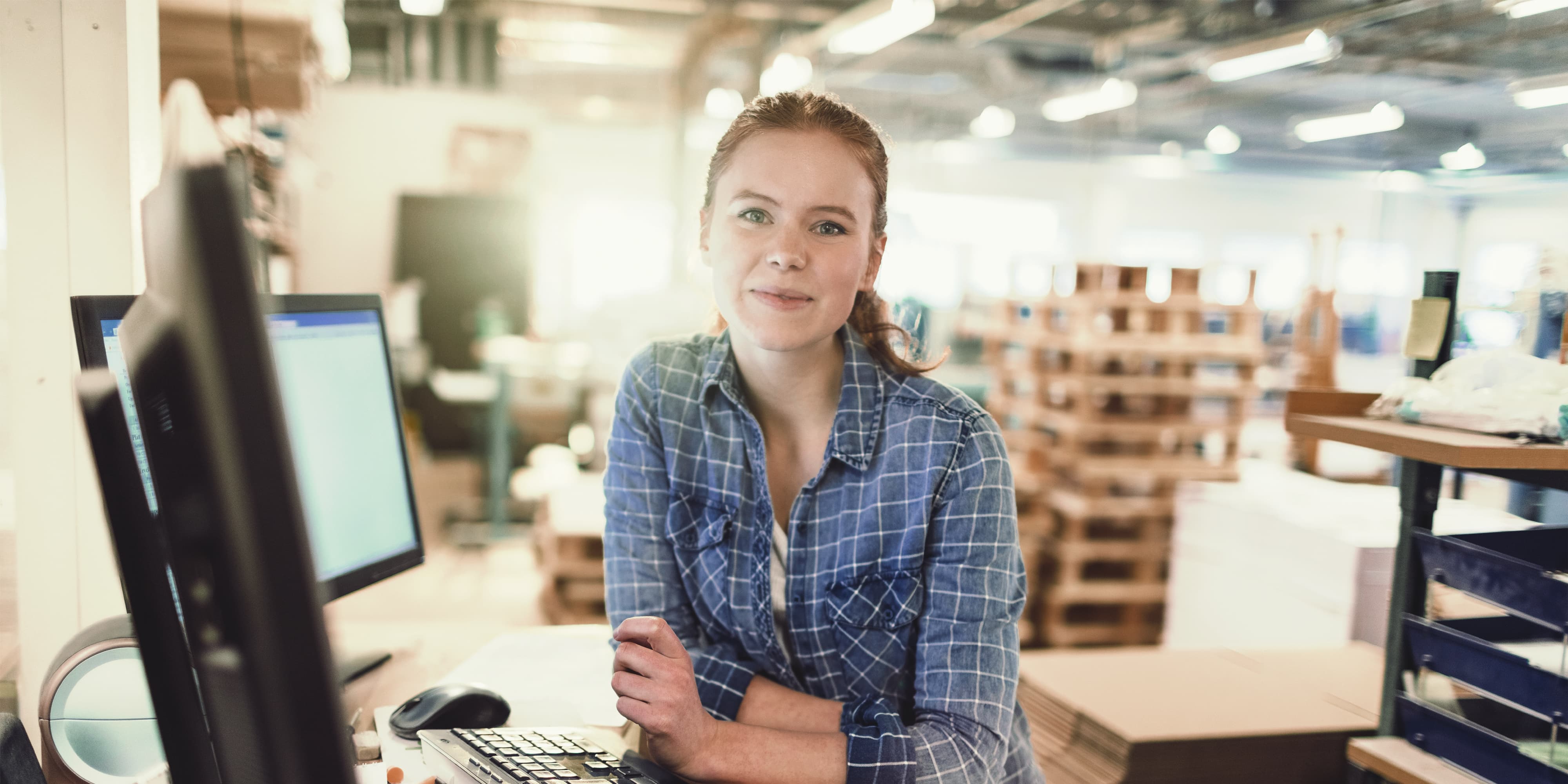 Frau arbeitet in Produktionshalle am PC