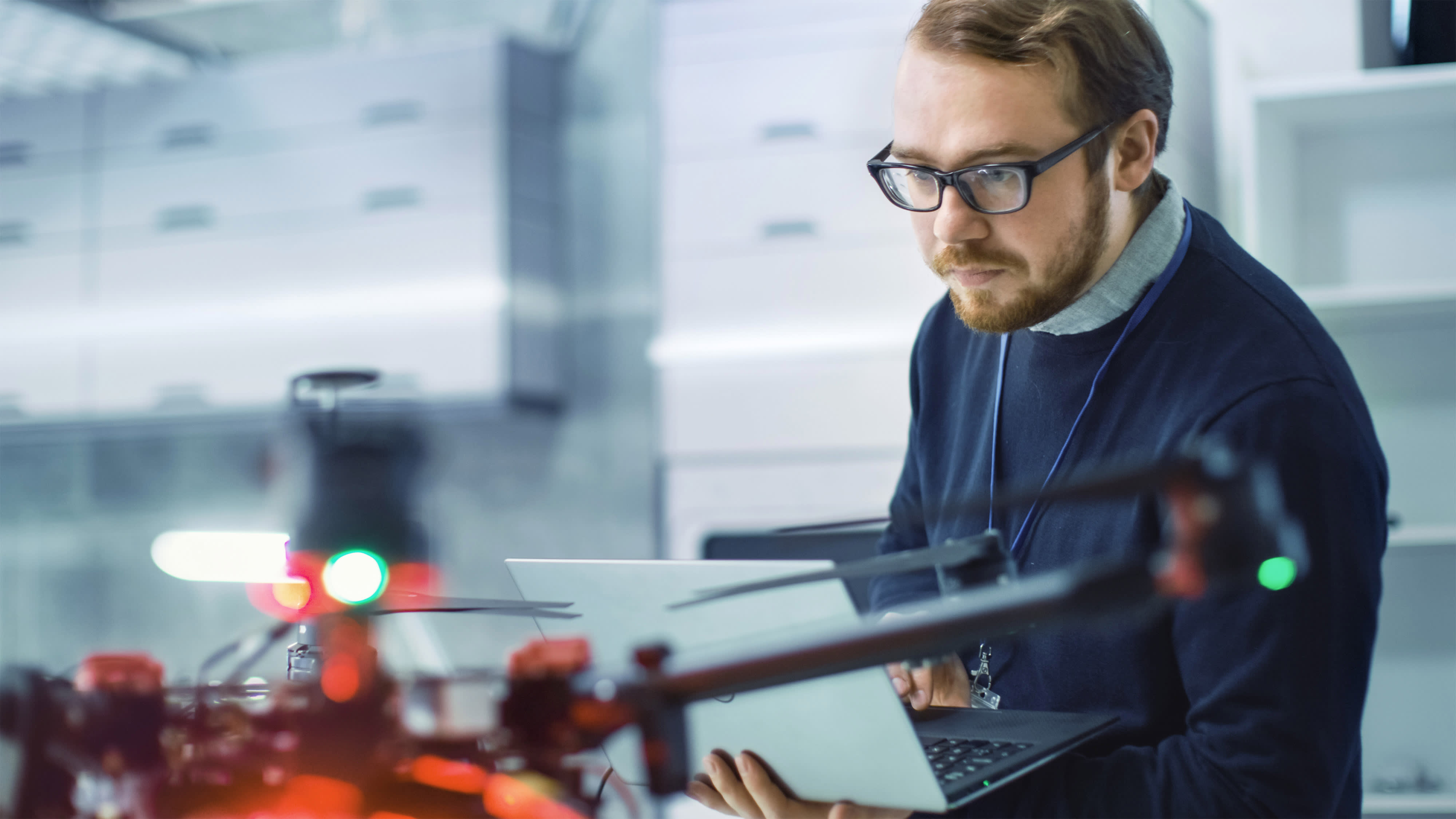 Male Engineer Programs Drone while Holding Laptop in His Hands.