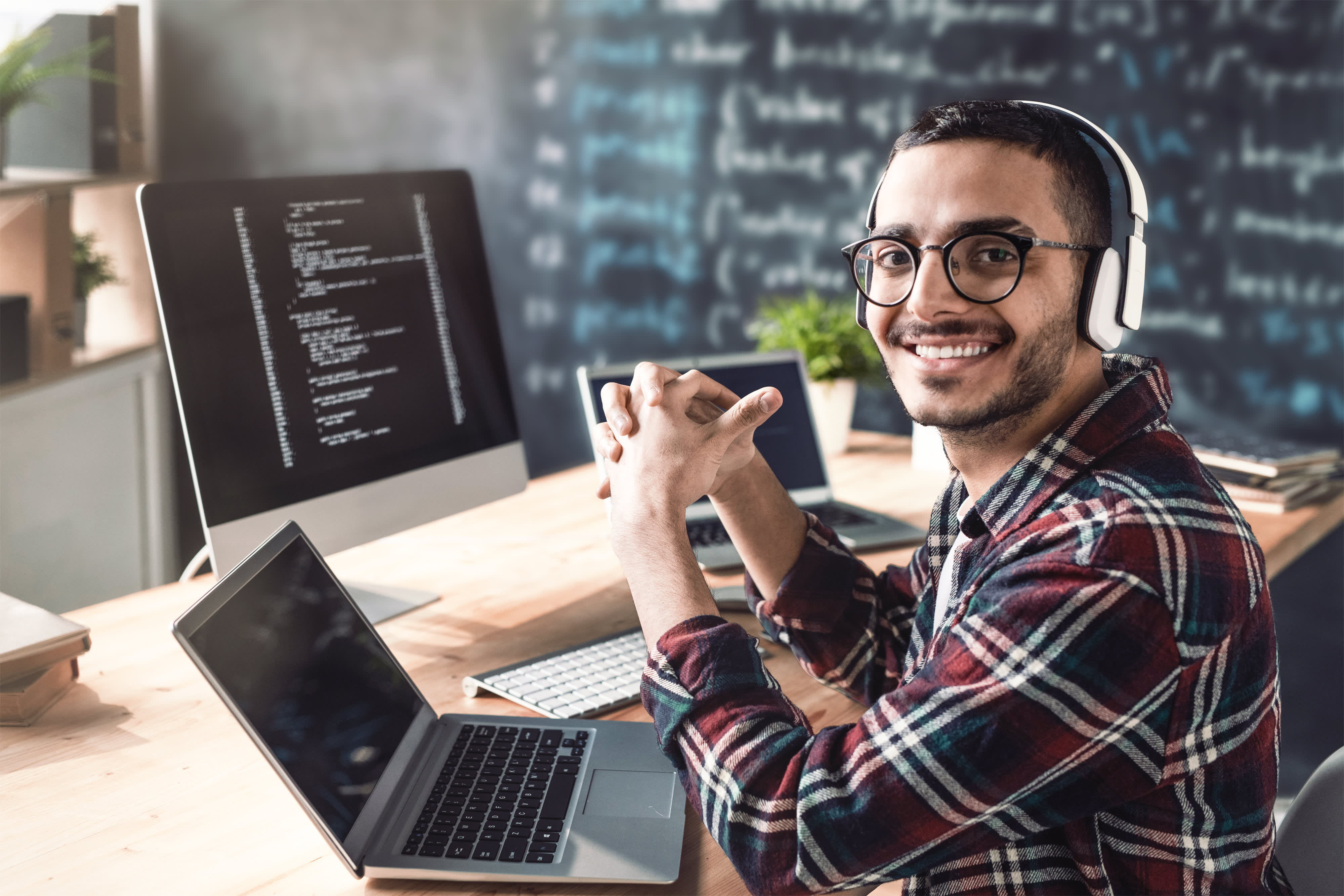 Junge fröhliche Programmierer mit Kopfhörern, die Sie mit einem Lächeln anschauen