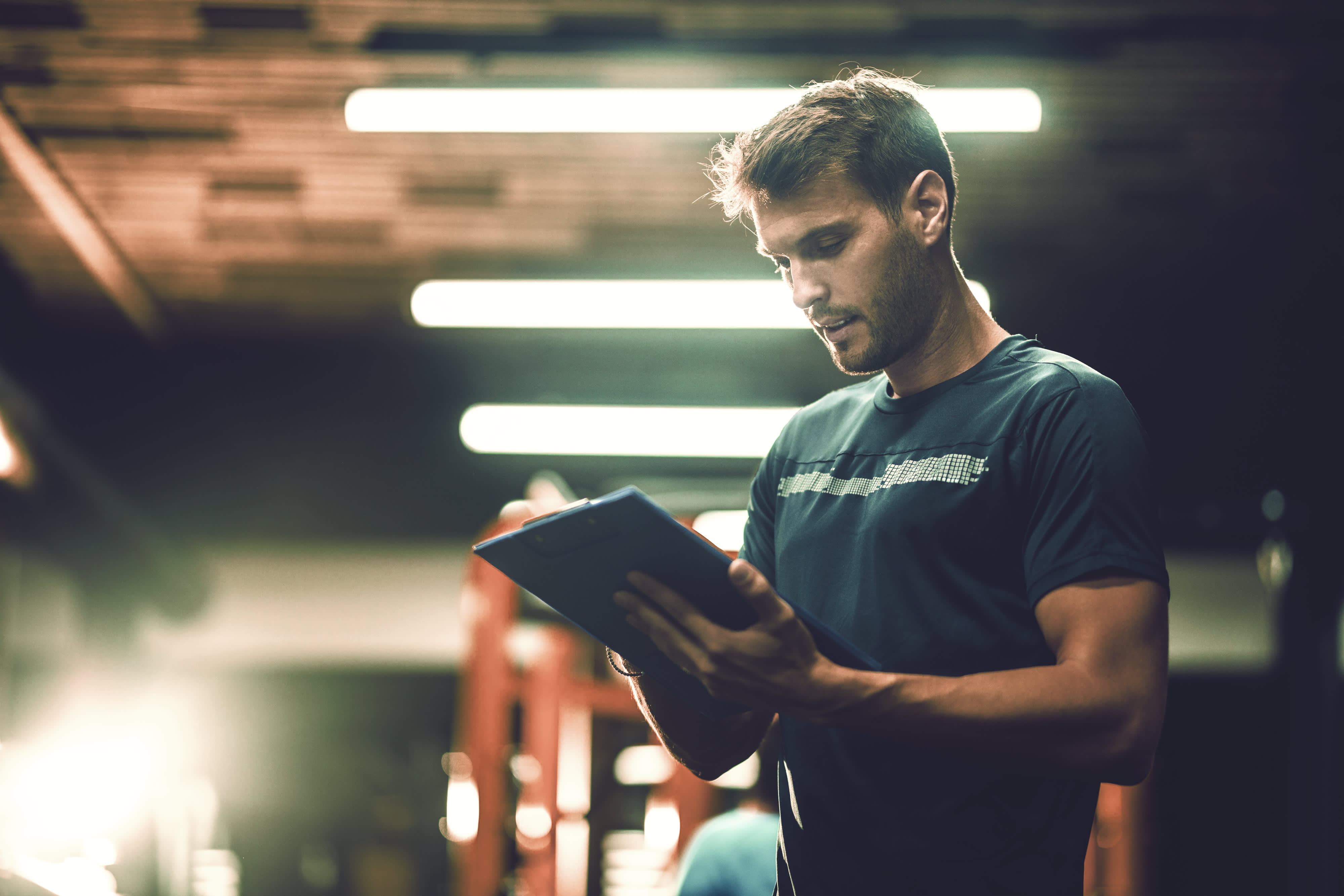 Junge Fitness-Trainer einen Trainingsplan in einem Fitnessstudio zu lesen