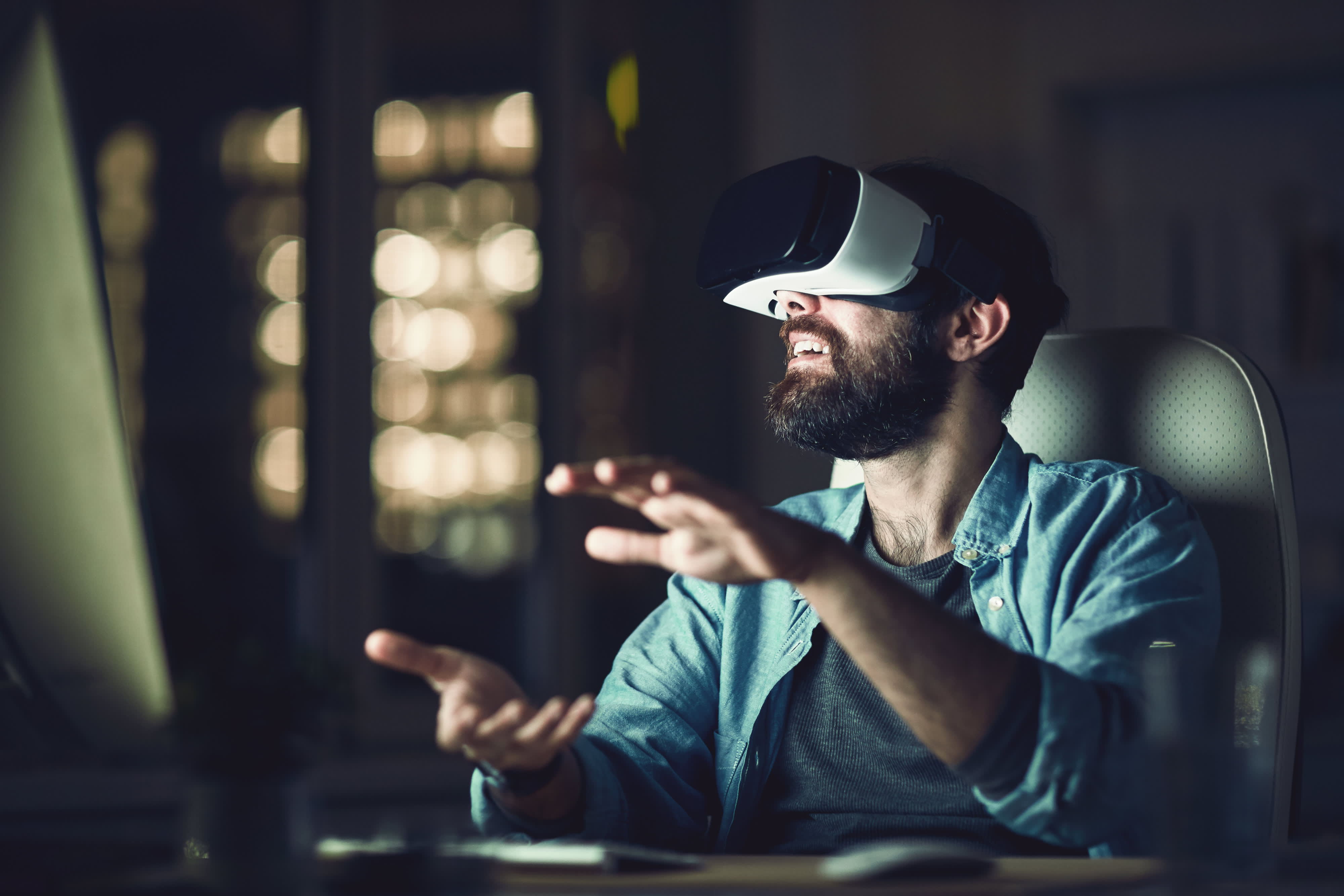 Aufgeregt junge bärtige Mann sitzt vor dem Computer und gestikulieren Hände beim Testen neue App über VR-Gerät