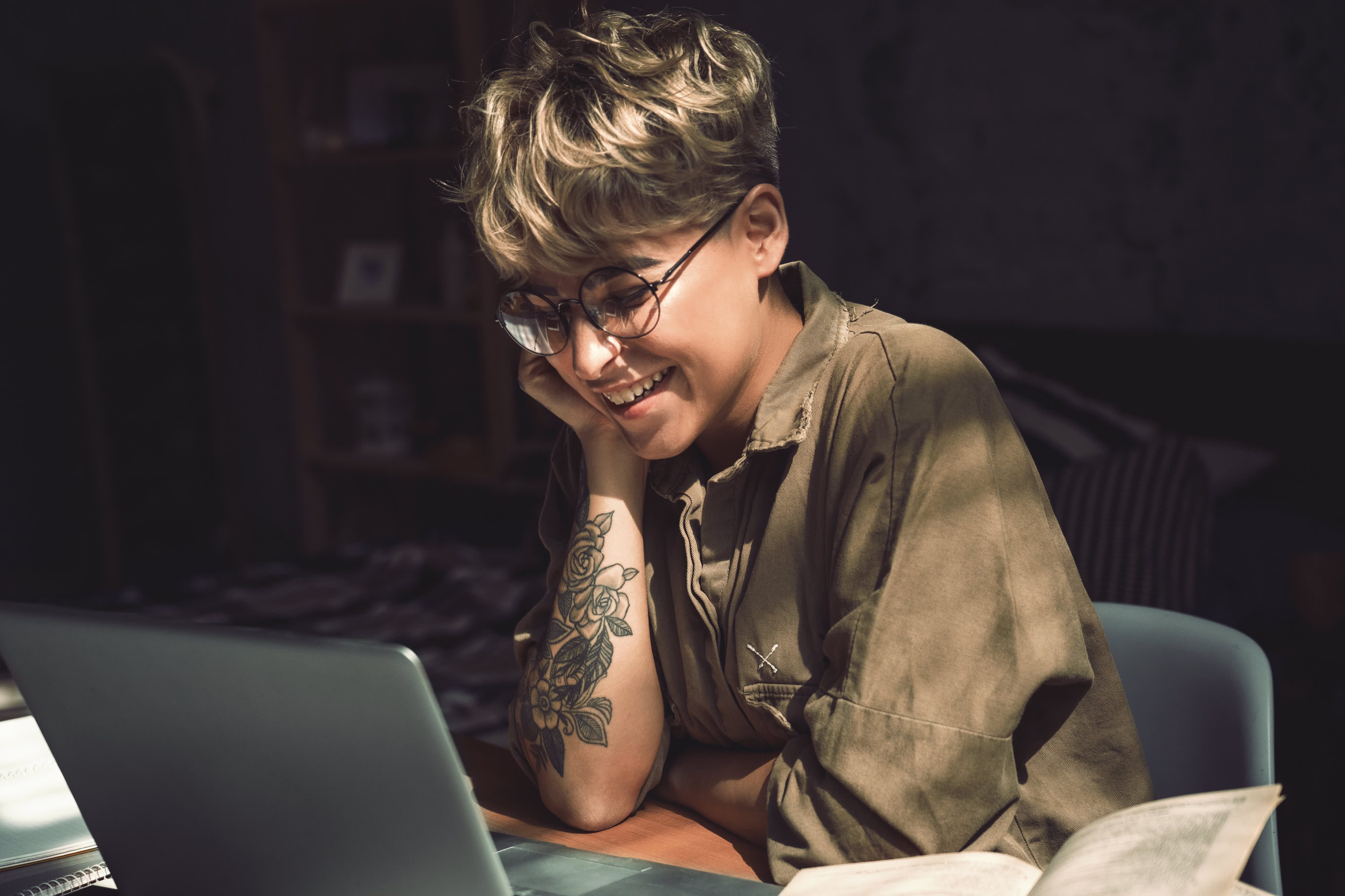 Junge Frau kurze Haare in Brille sitzt am Schreibtisch studieren online auf Laptop Blick auf Bildschirm lachen fröhlich