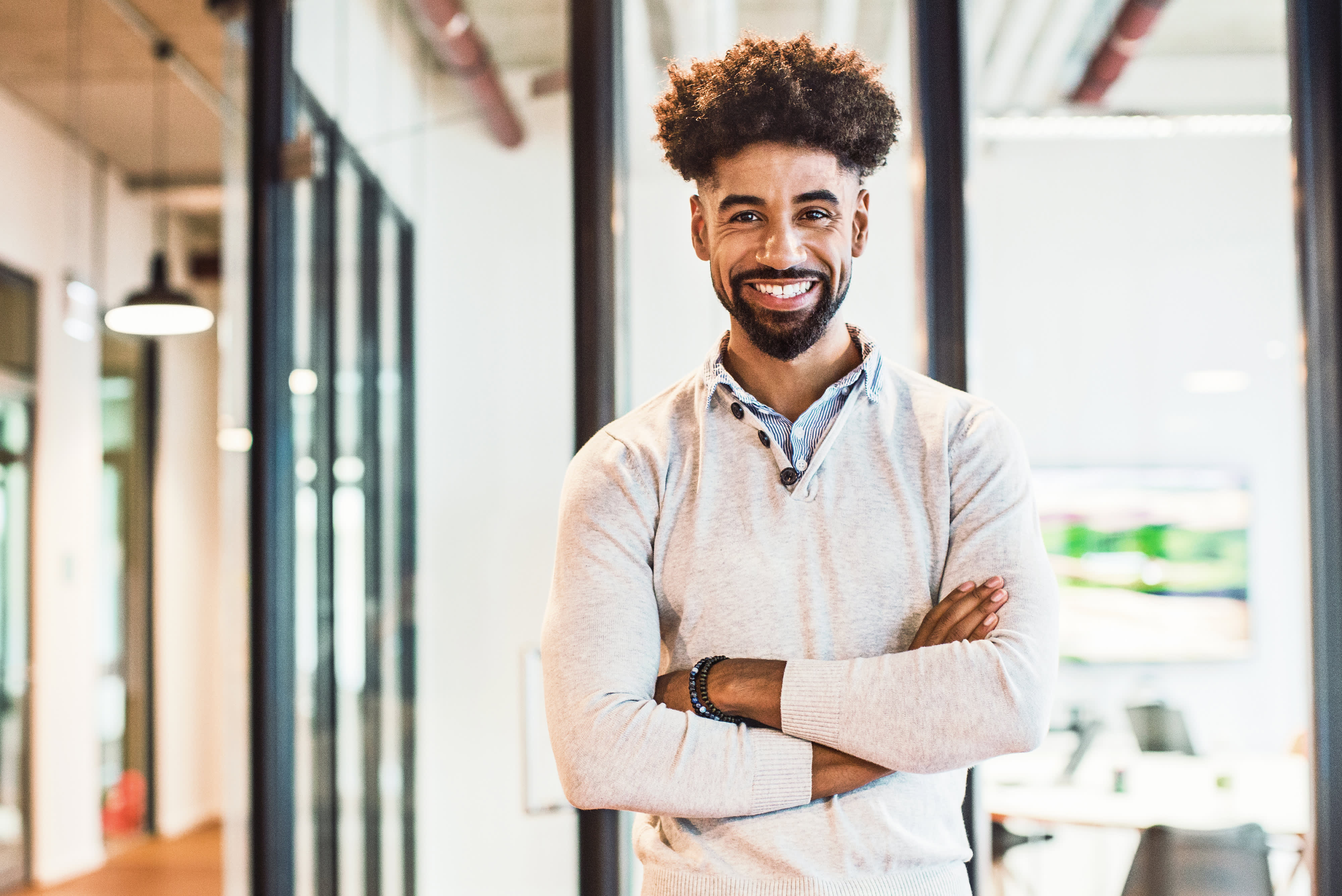 Smiling young businessman standing arms crossed in office