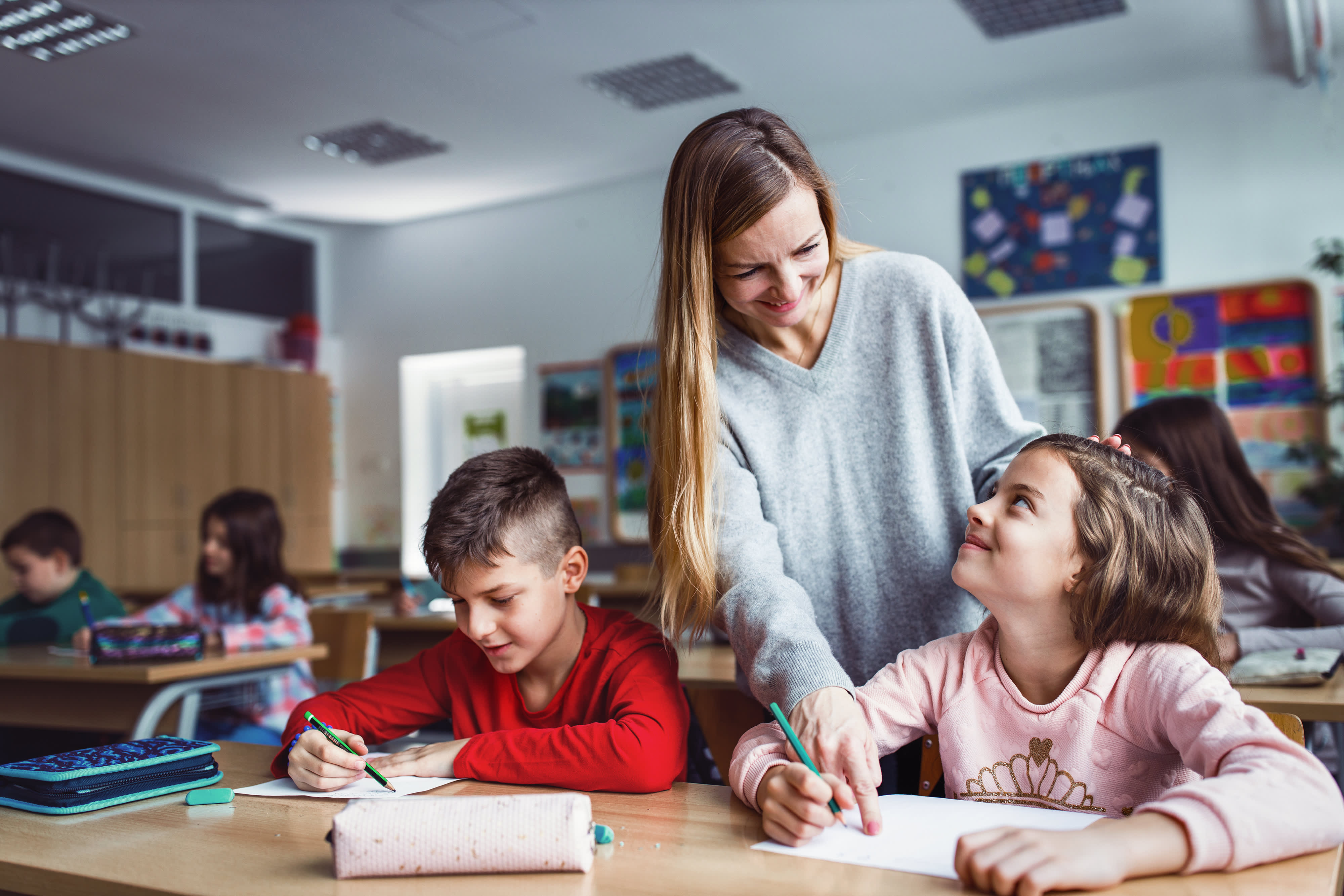 Glückliche Grundschullehrerin im Gespräch mit Kindern im Klassenzimmer