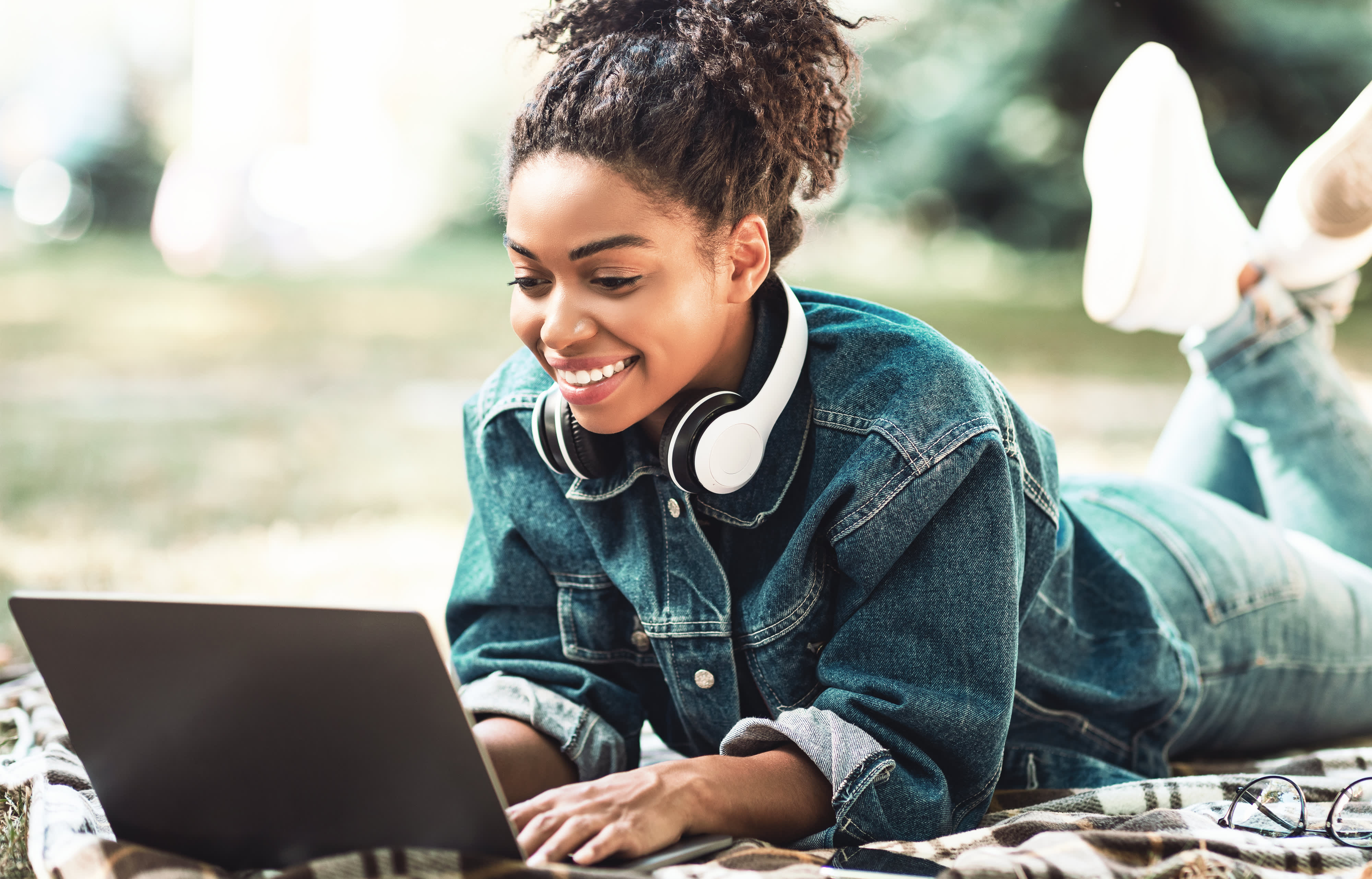 Afrikanische Frau, die am Laptop arbeitet und im Park liegt