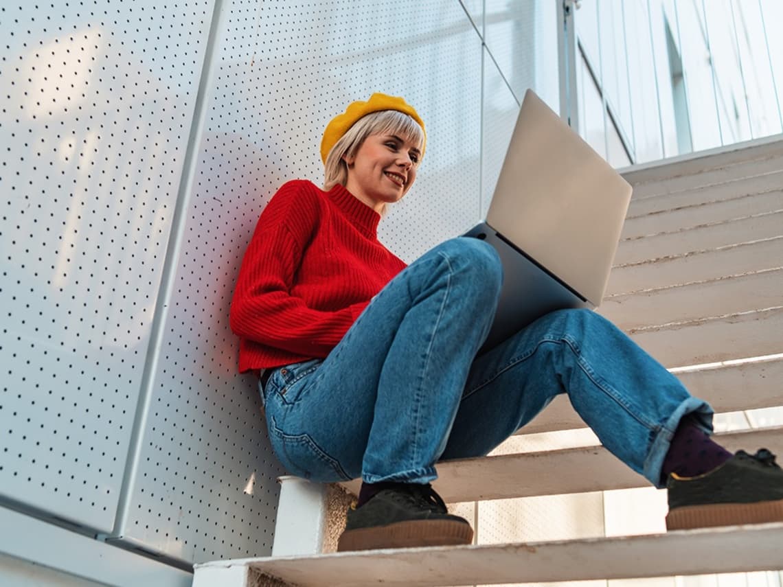 Studieninteressierte sitzt auf einer Treppe mit ihrem Laptop auf den Knien und informiert sich über ein duales Studium ohne Abitur.