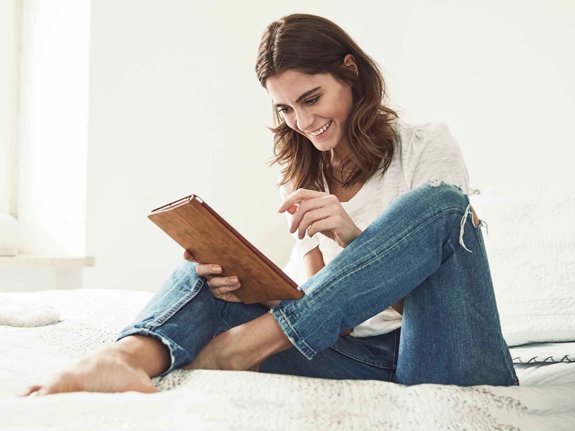 Titelbild für Infoseite "Duales Studium Nebenjob": Duale Studentin sitzt auf dem Bett mit Tablet in der Hand