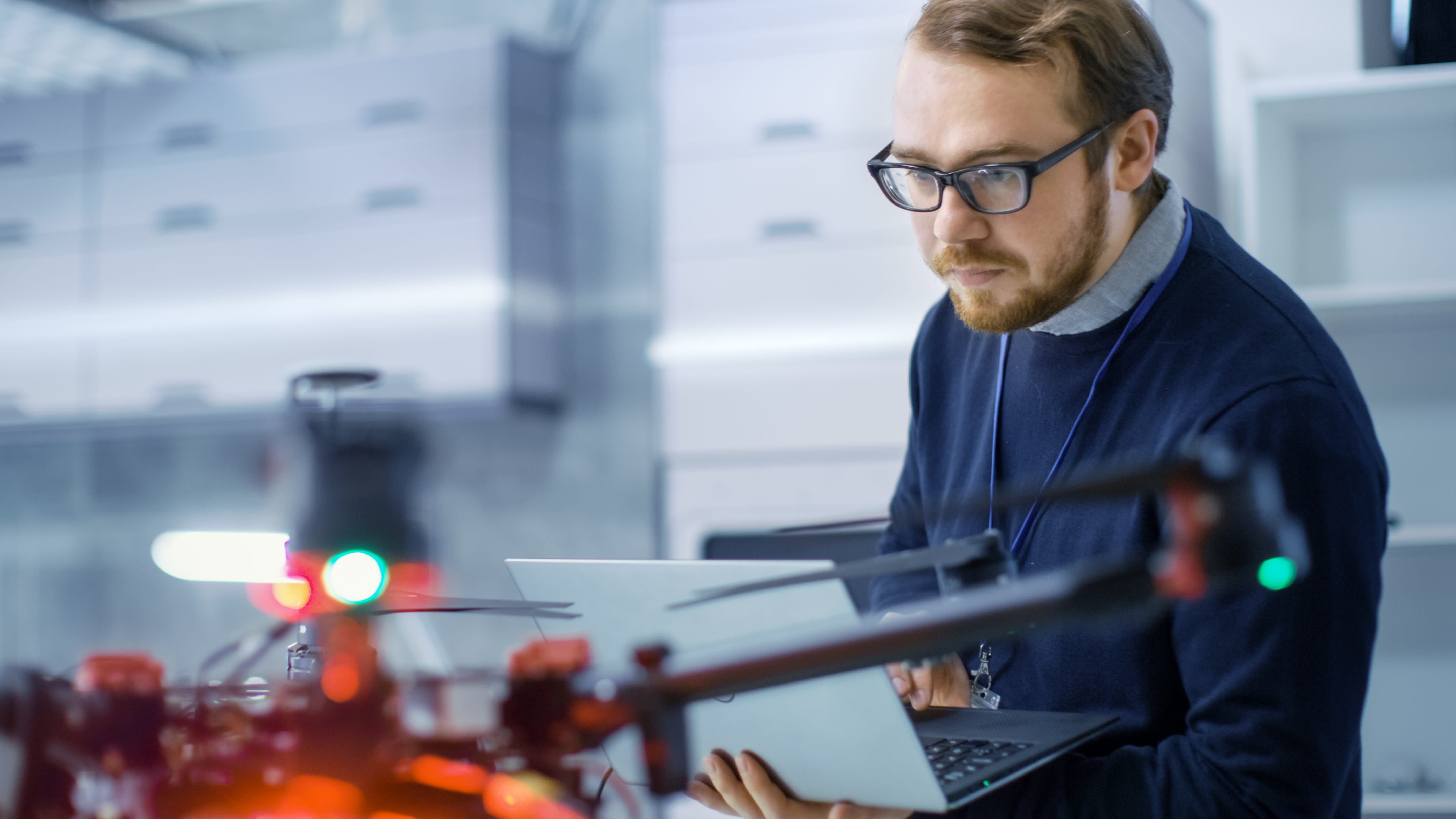 Titelbild für Infoseite “Bachelor Angewandte Künstliche Intelligenz”: Student arbeitet an einer Drohne mit Laptop in der Hand