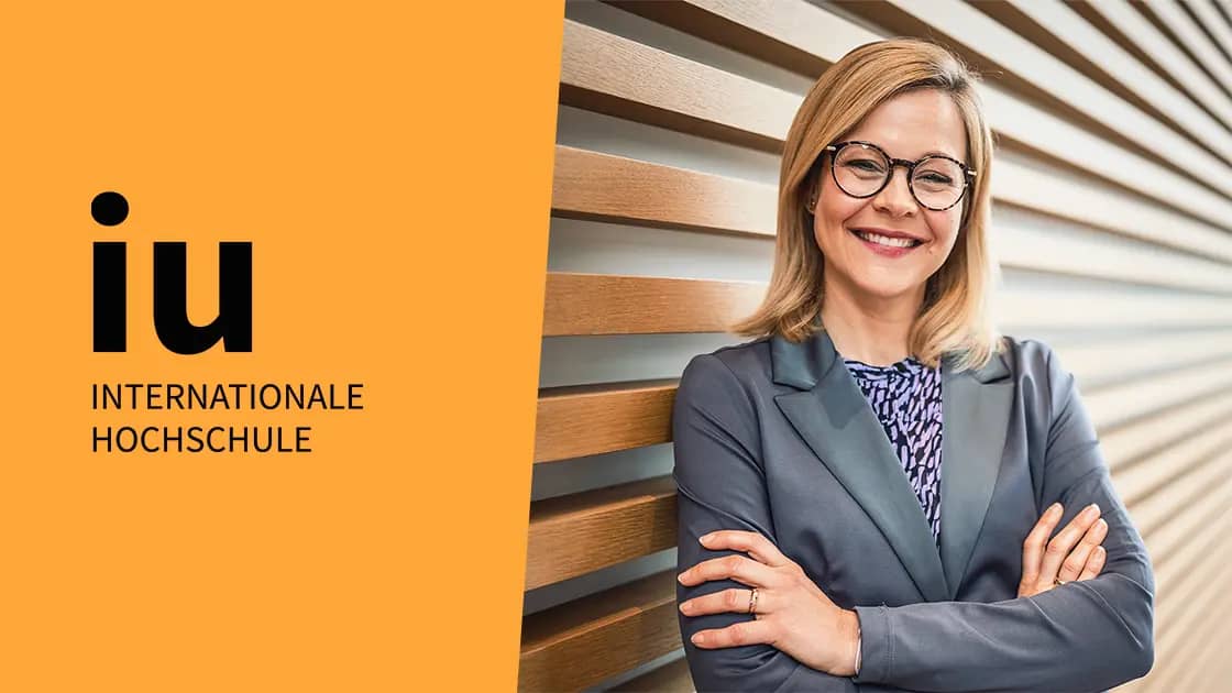 Titelbild zum Artikel: "IU Vortrag - Werde zur Heldin Deiner Gründung: Sabrina Micklich, Projektleiterin für Entrepreneurship & Innovation an der IU Internationalen Hochschule, steht lächelnd vor einer holzgetäfelten Wand