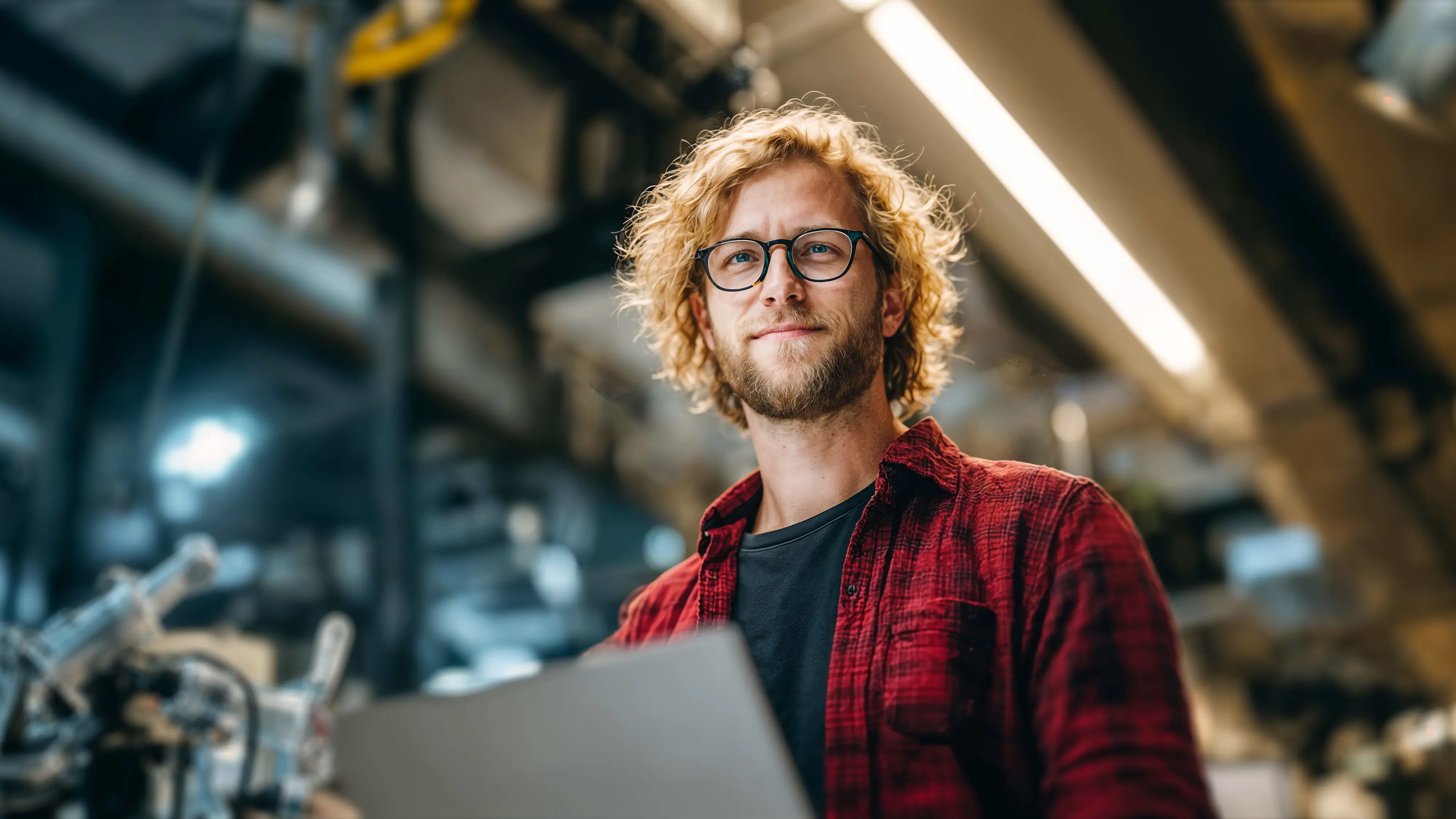 Bachelor Applied Artificial Intelligence: Mann steht mit Tablet in einer Werkshalle mit Robotik, AI-generated