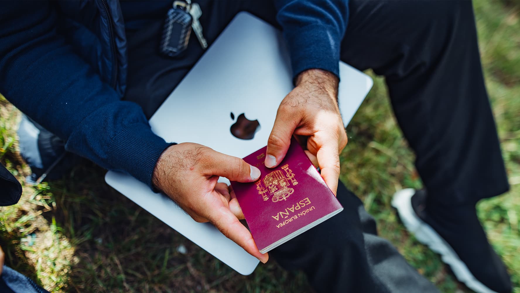 Man hands holding a Spanish passport and a laptop