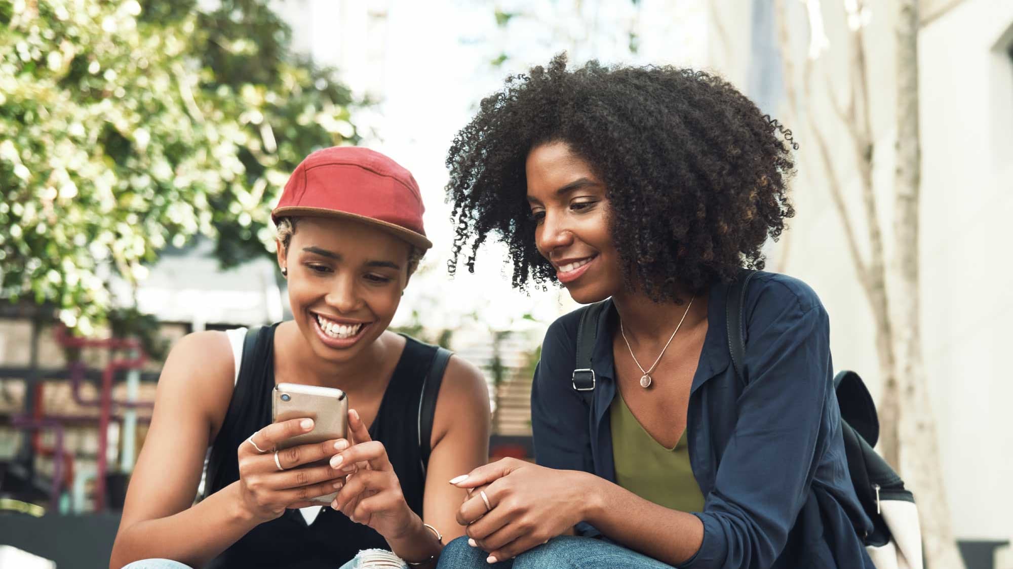 Titelbild für Infoseite “Hochschulwechsel”: Zwei Studentinnen sitzen draußen und schauen gemeinsam auf ein Smartphone