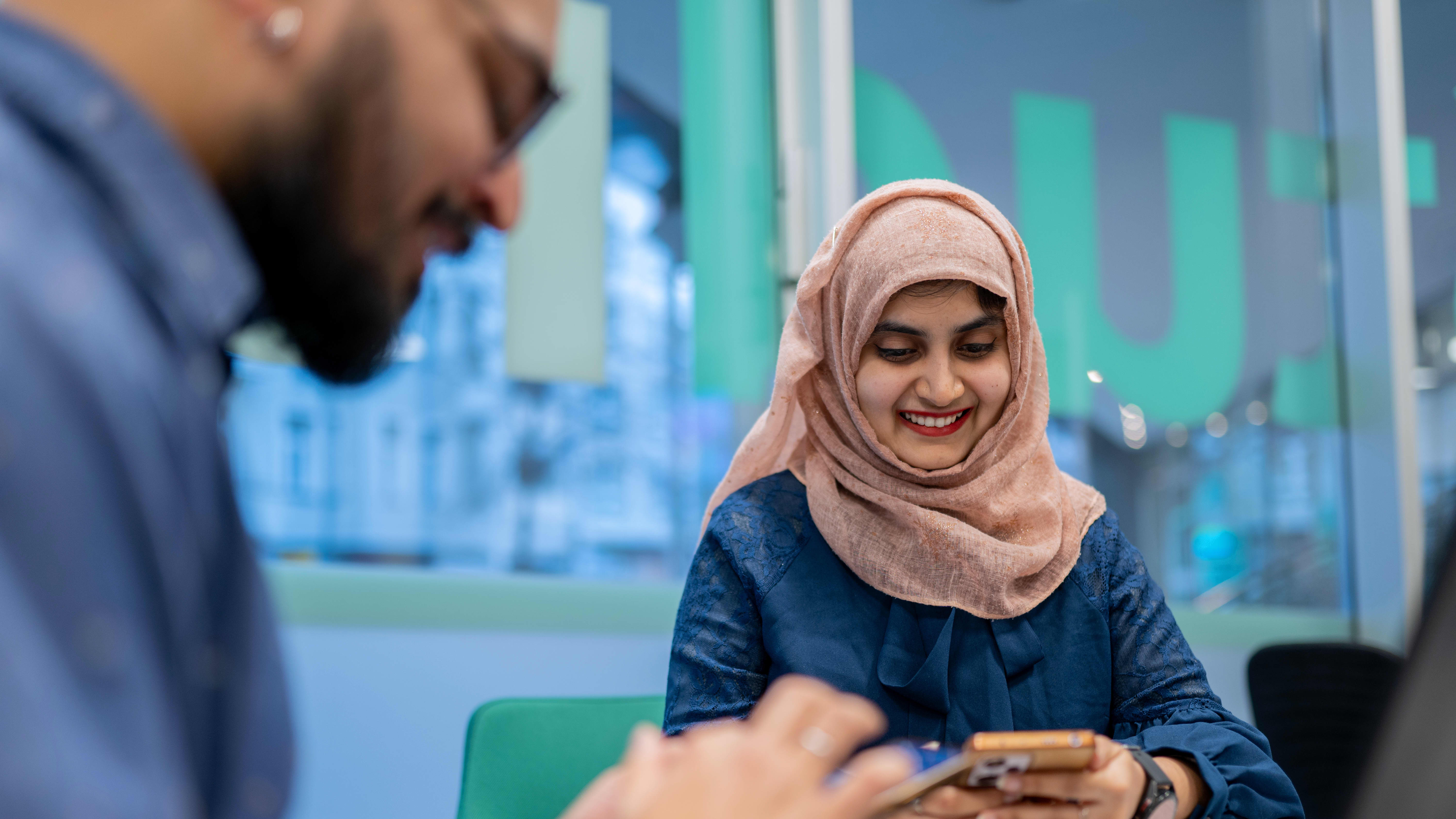 A girl wearing a hijab and a guy next to her, are checking their phones