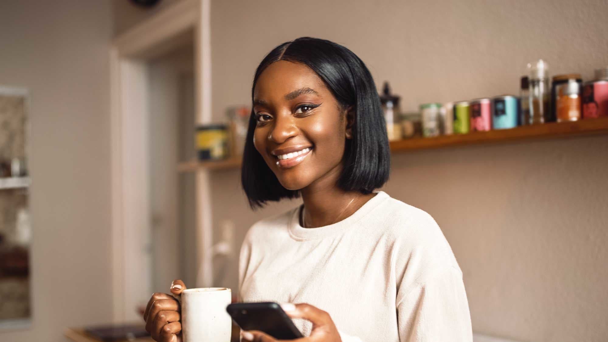 Lächelnde Studentin mit Kaffee und Smartphone in der Hand