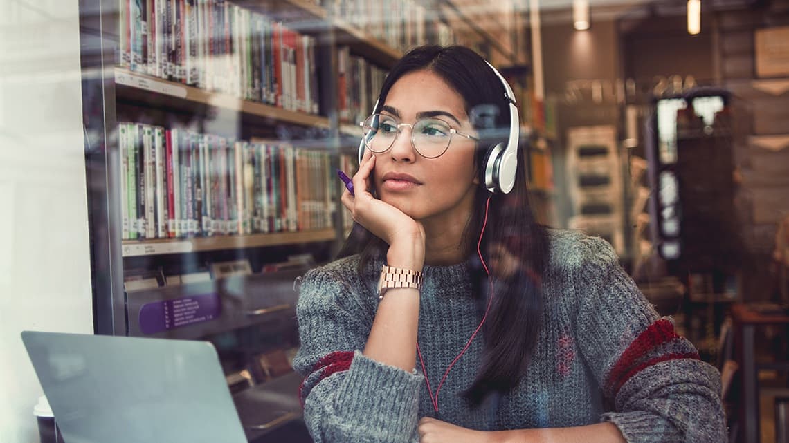 Studentin mit Laptop und Kopfhörer in Bibliothek