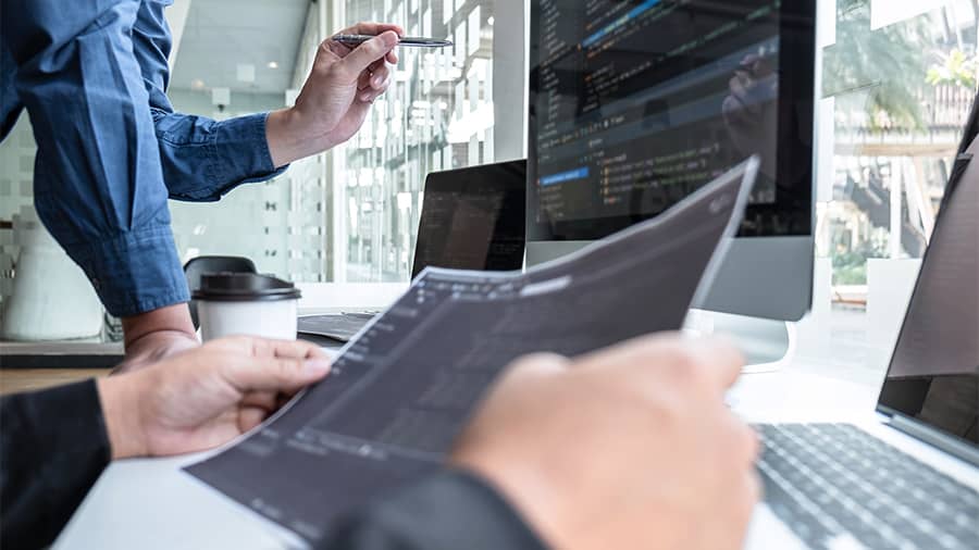 Men in an office holding a paper and doing data analysis
