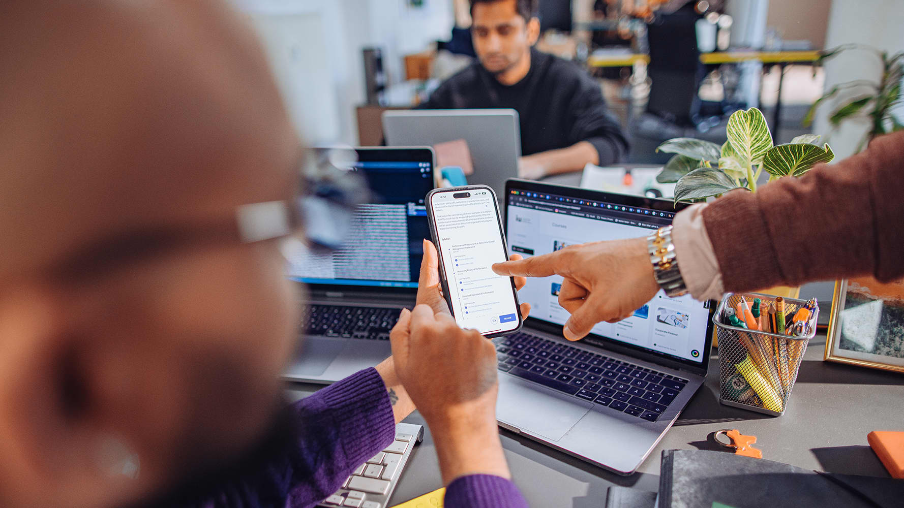 Students observing a mobile phone while working with multiple screens