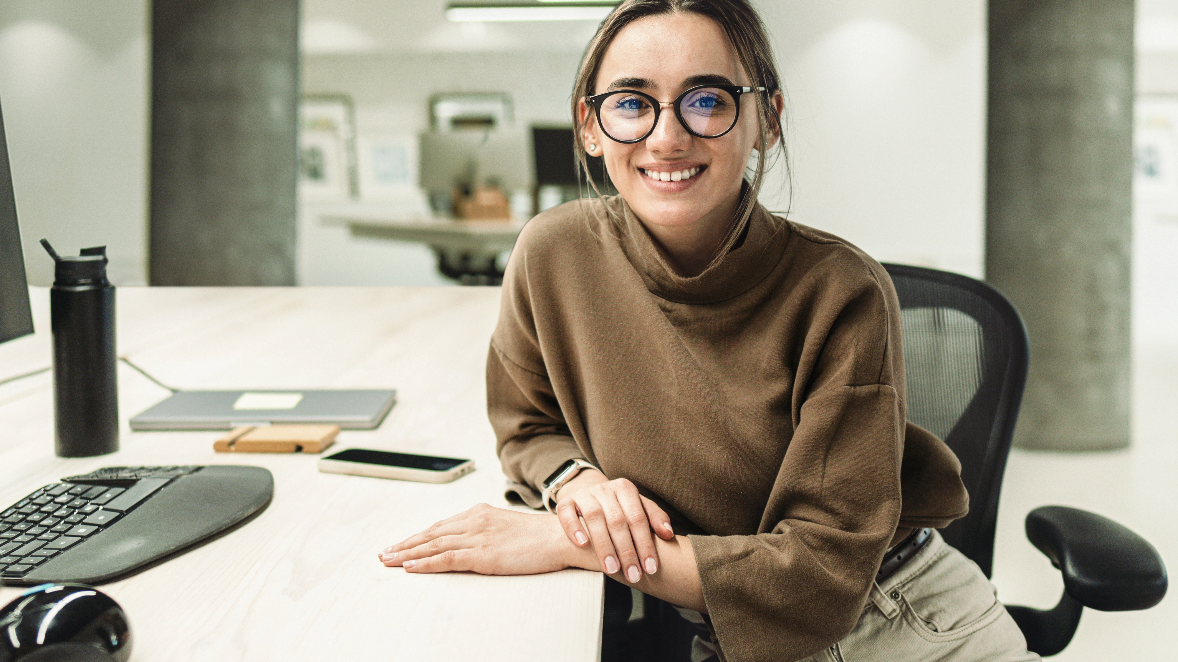Woman, with glasses, sitting in an office and smiling to the camera
