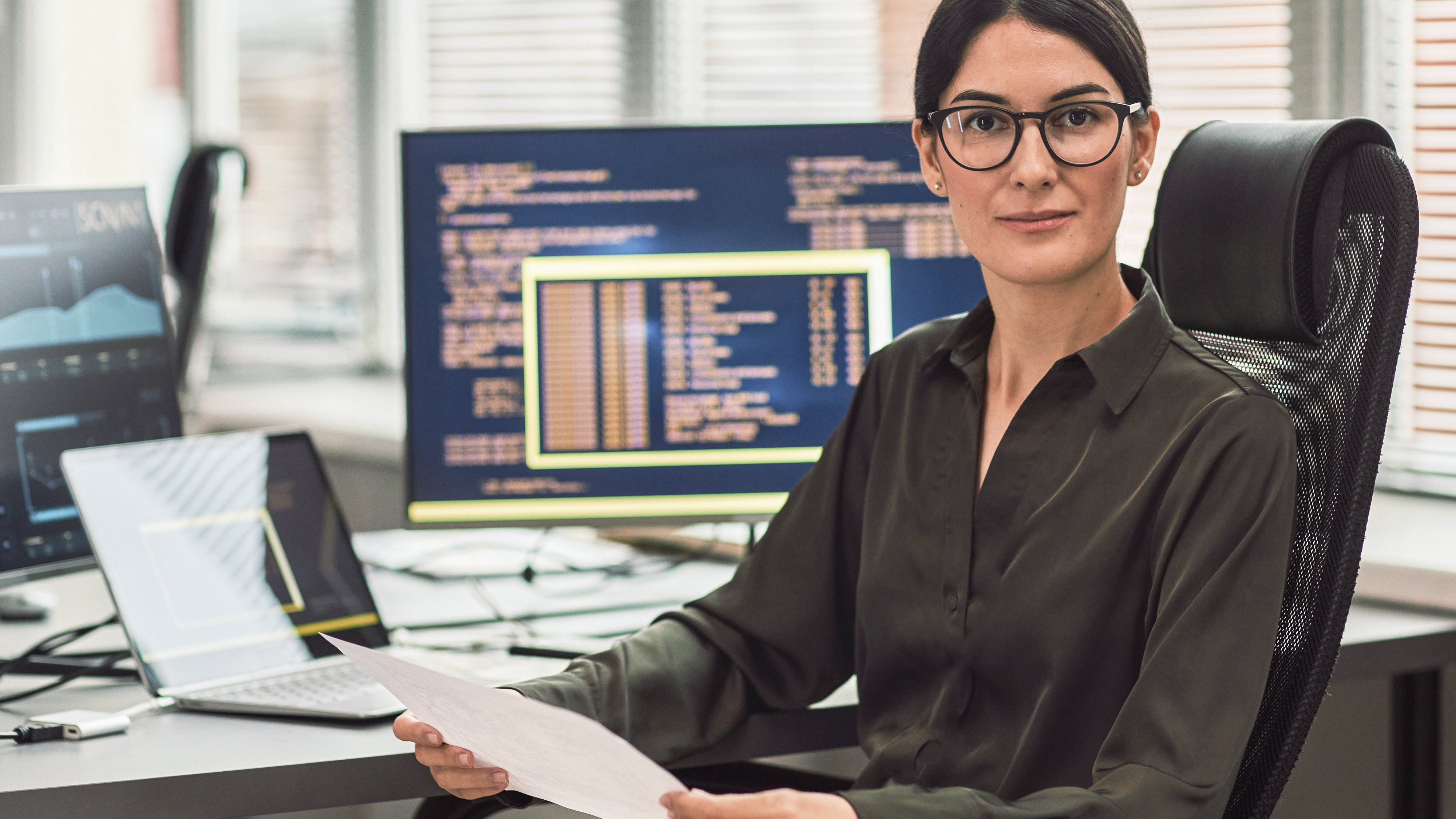 Serious woman holds a paper and looks at the camera while sitting in an office