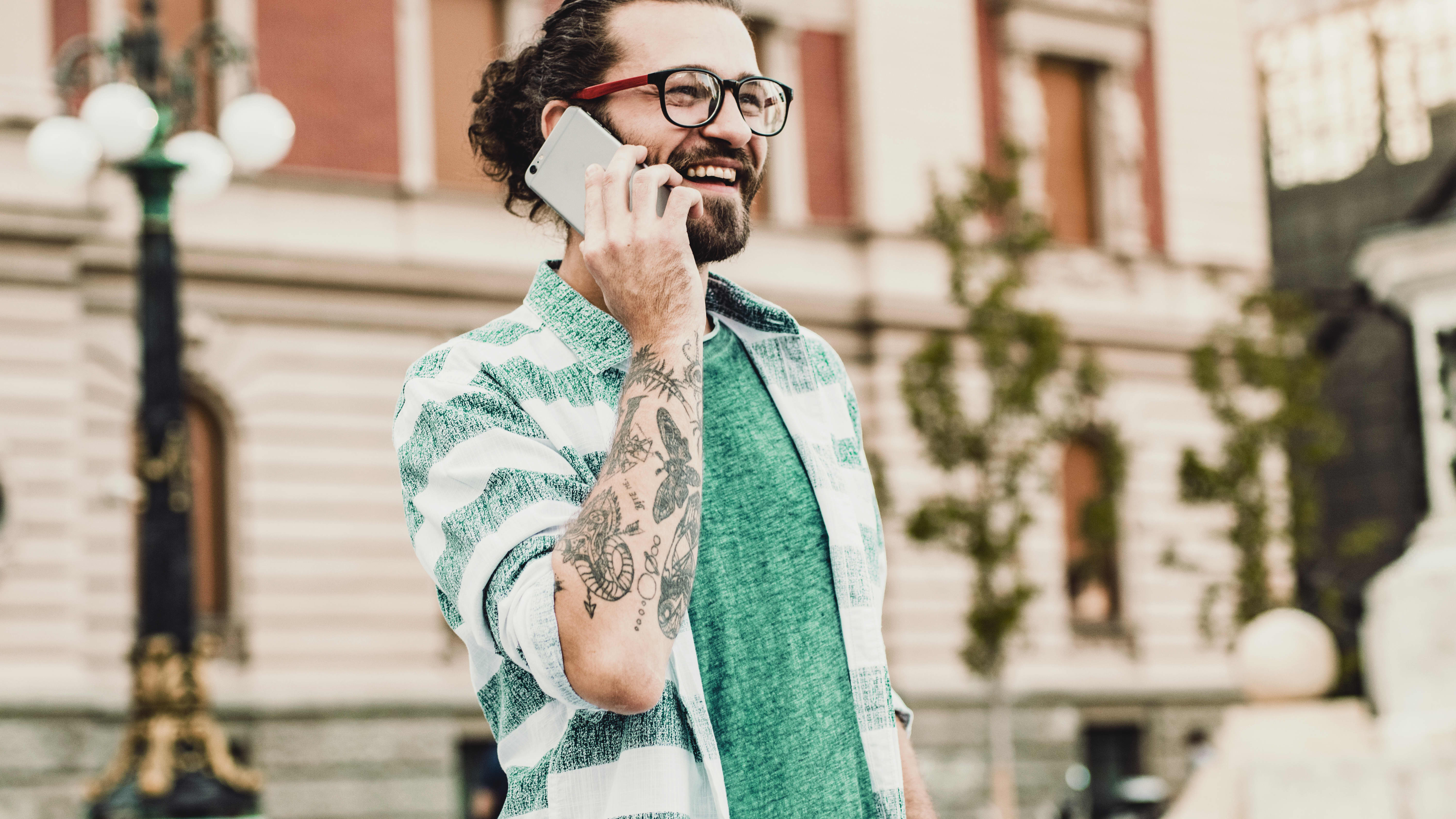 Man wearing glasses and with tattoos, speaks on the phone on the street