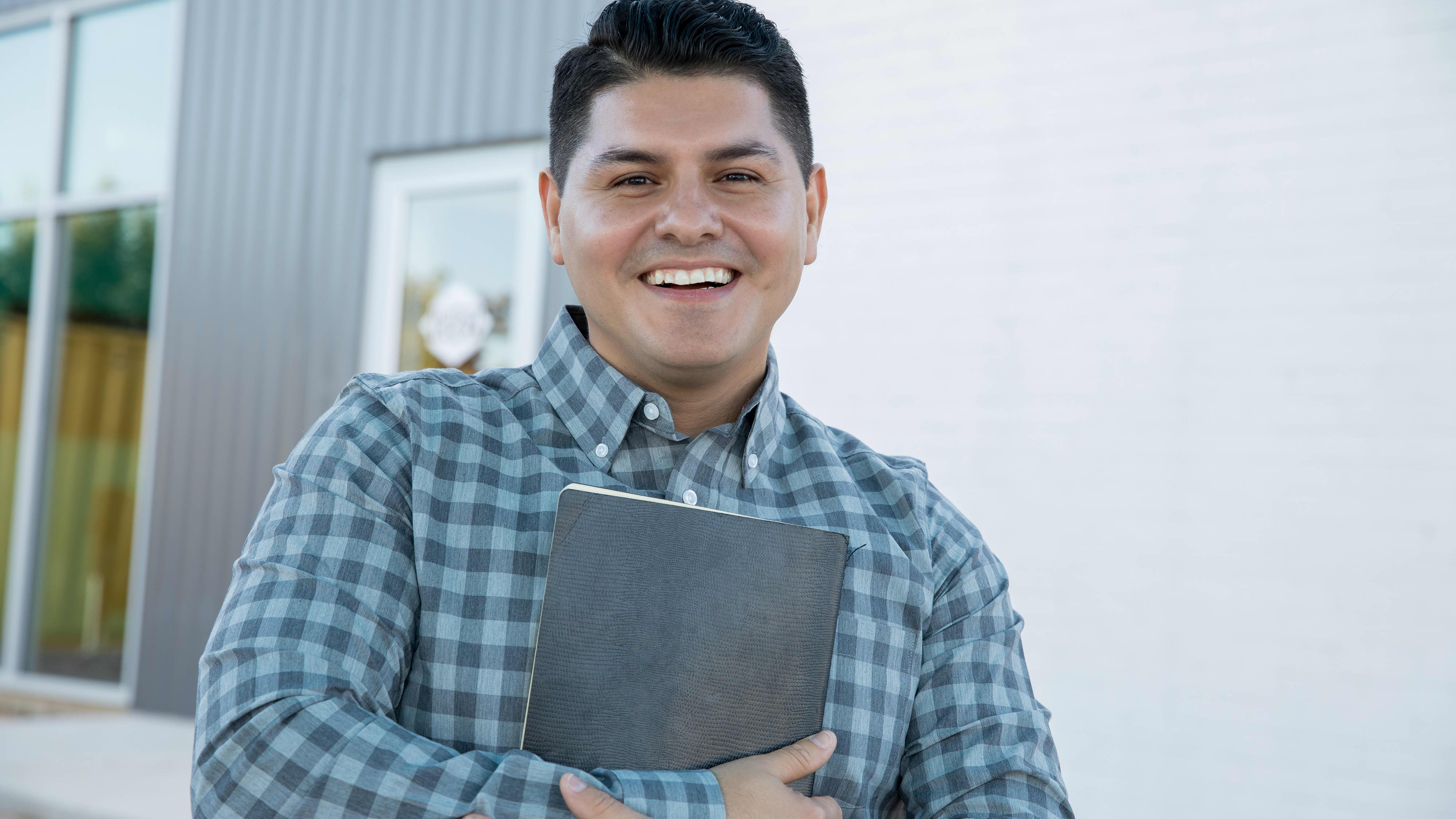 Man wearing a checked shirt, smiles to the camera while holding a book