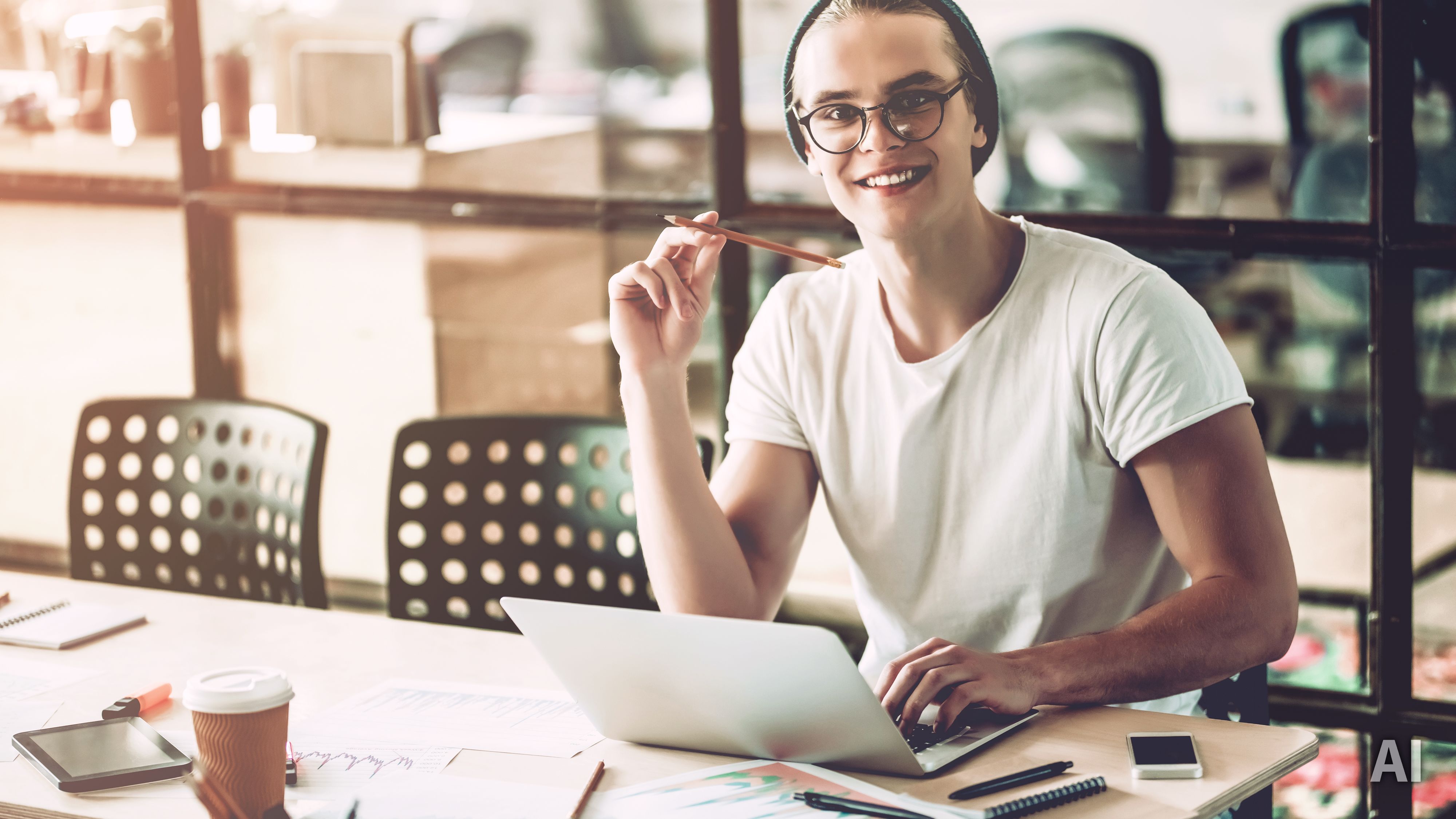 Titelbild für Infoseite “duales Studium Marketingmanagement": Lächelnder Student am mit Laptop am Schreibtisch, AI-generated