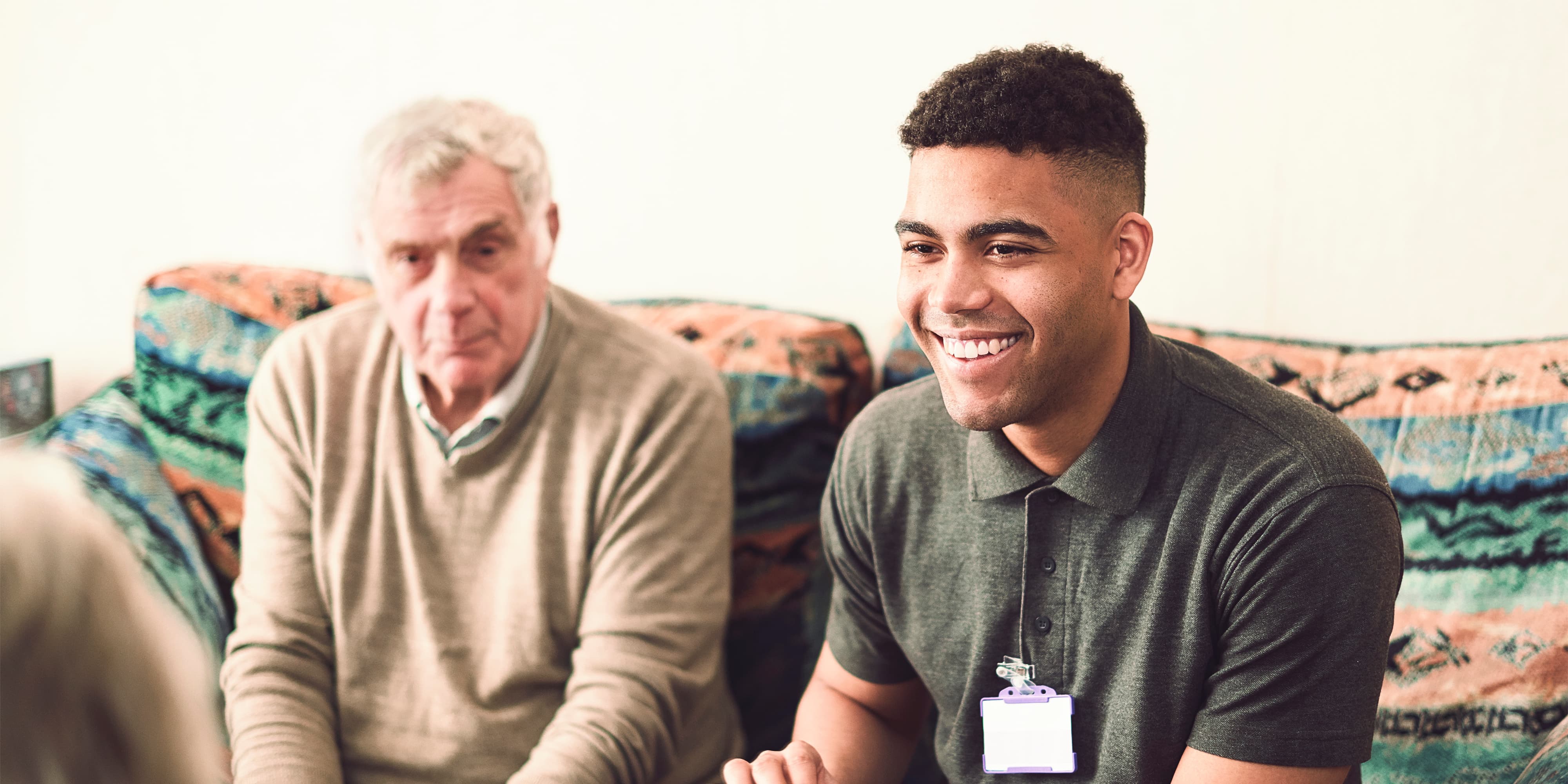 Titelbild für Infoseite “Bachelor Gerontologie”: Gerontologie-Student spricht mit Patienten im Wohnzimmer