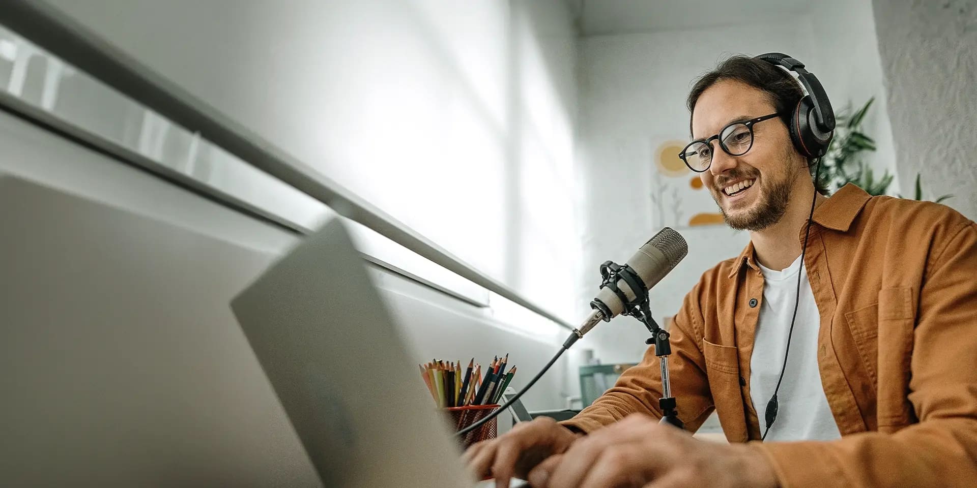 Titelbild zum Artikel "Journalis:in werden": Journalist sitzt am Laptop mit Mikrofon und Headset