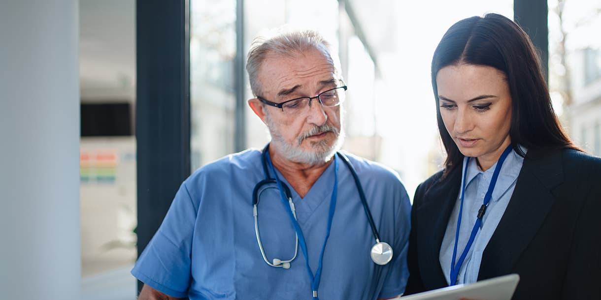 A healthcare professional in a blue uniform and stethoscope collaborates with a businessperson holding a tablet, illustrating teamwork in mba in healthcare management in Germany.