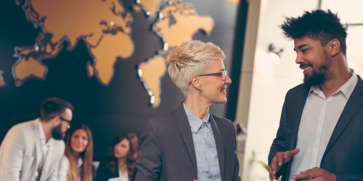 Two business professionals engage in a discussion with a world map in the background, representing the concept of international management in Germany.
